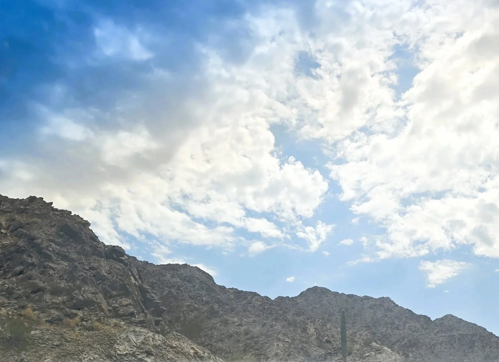 A rugged mountain slope at the bottom with rocky terrain, and a bright sky above with scattered clouds.