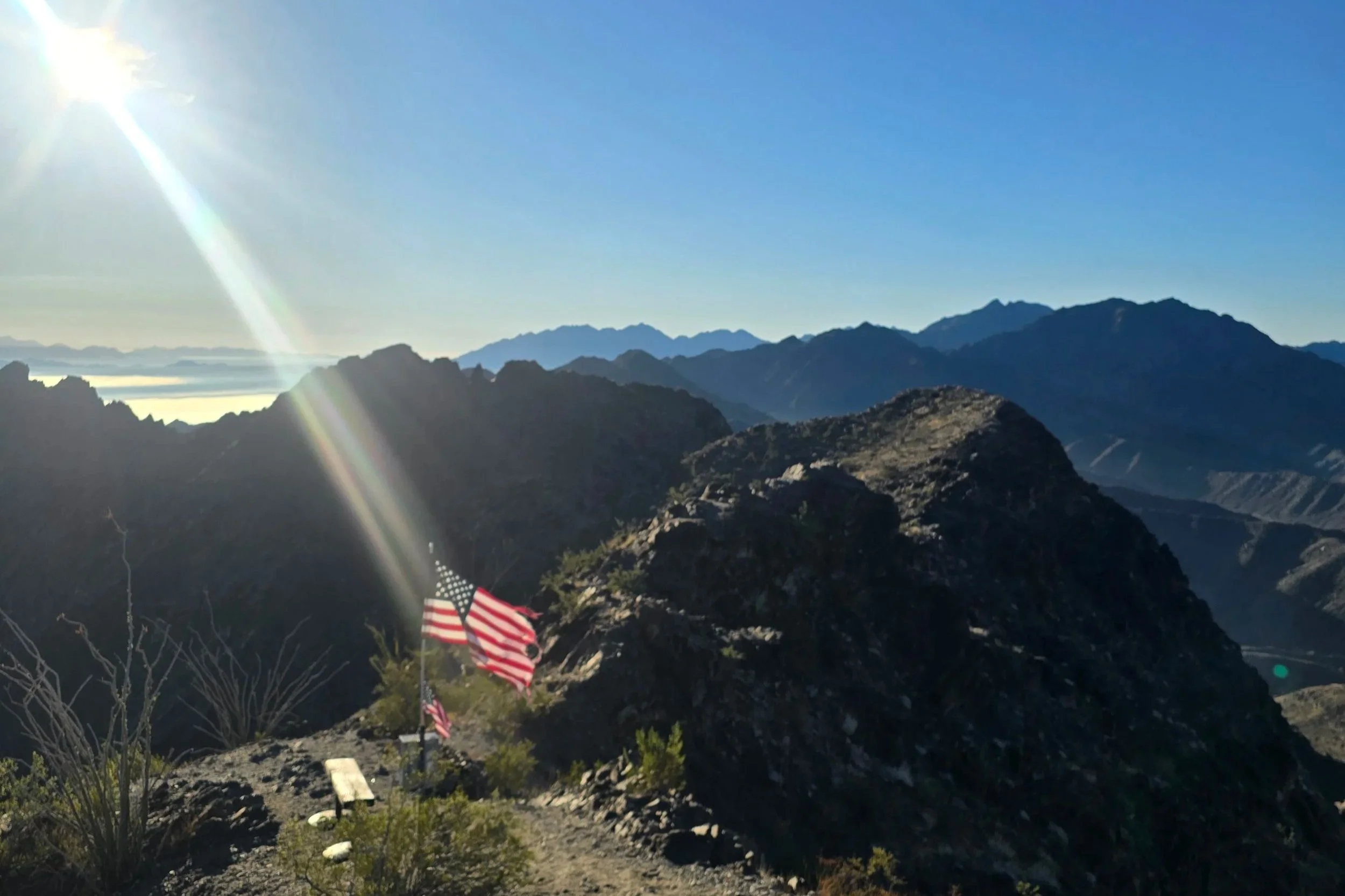 Mountain landscape with clear blue sky, sunlight, and American flags in the foreground.