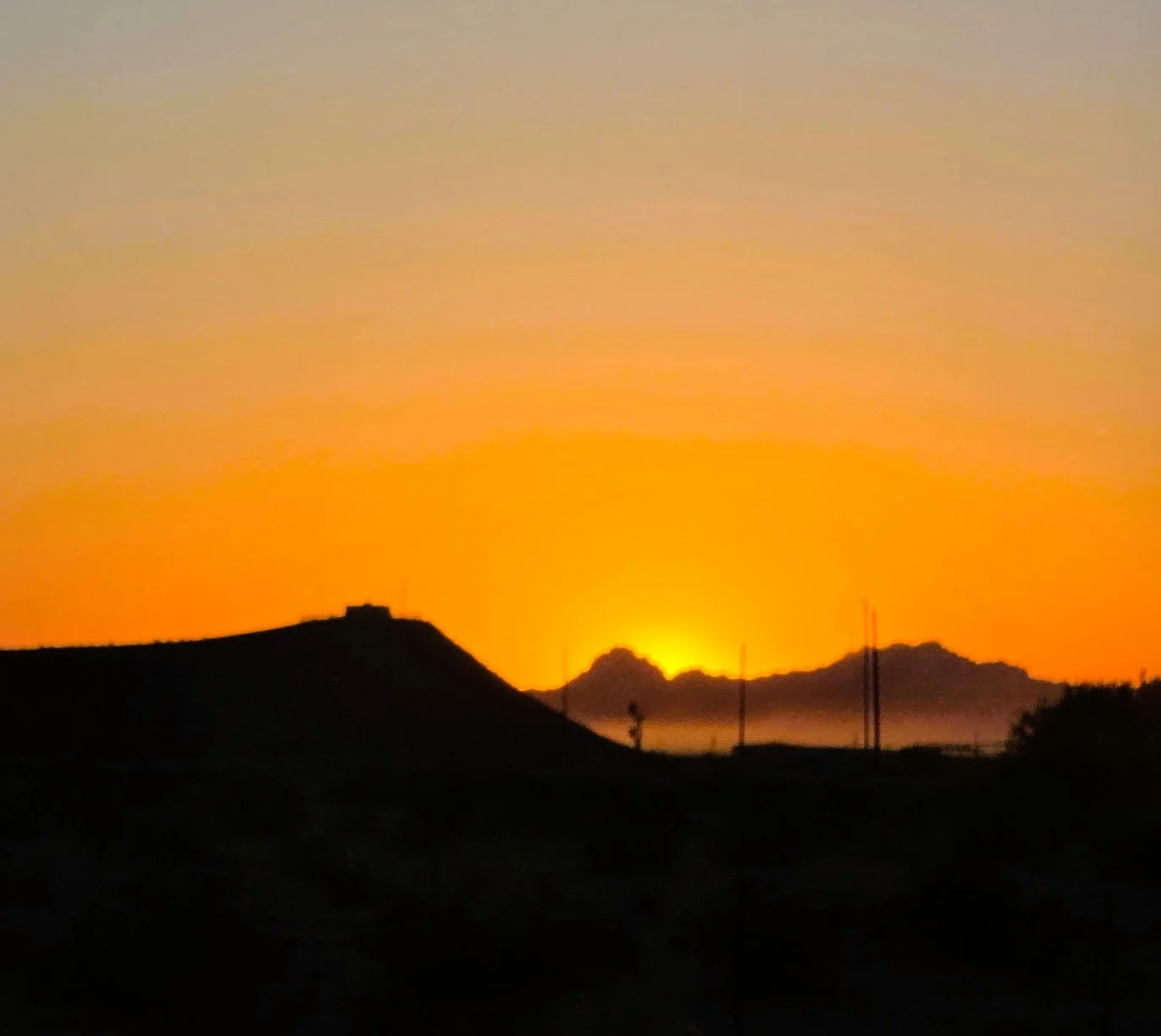 Sunset behind mountain silhouette with colorful sky and distant power lines.