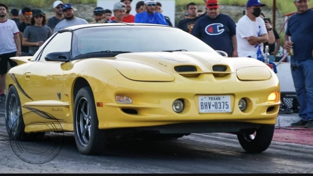 Yellow sports car on a drag strip with spectators in the background.