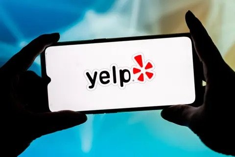 Person holding a smartphone with the Yelp logo on the screen.