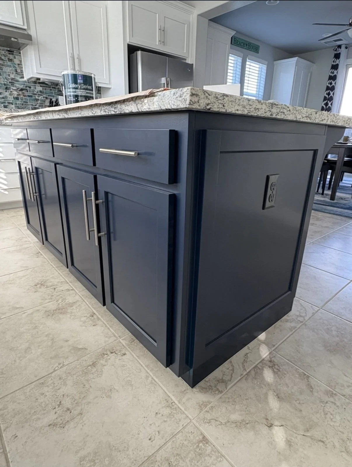 Kitchen island with dark blue cabinets, granite countertop, and electrical outlet on the side, located in a modern kitchen with light-colored flooring and white cabinets.
