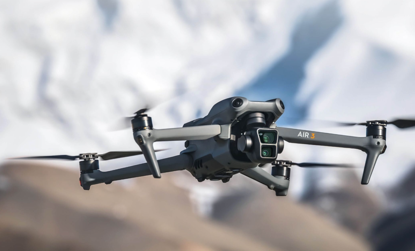 A drone flying in the air over a snowy mountain landscape.