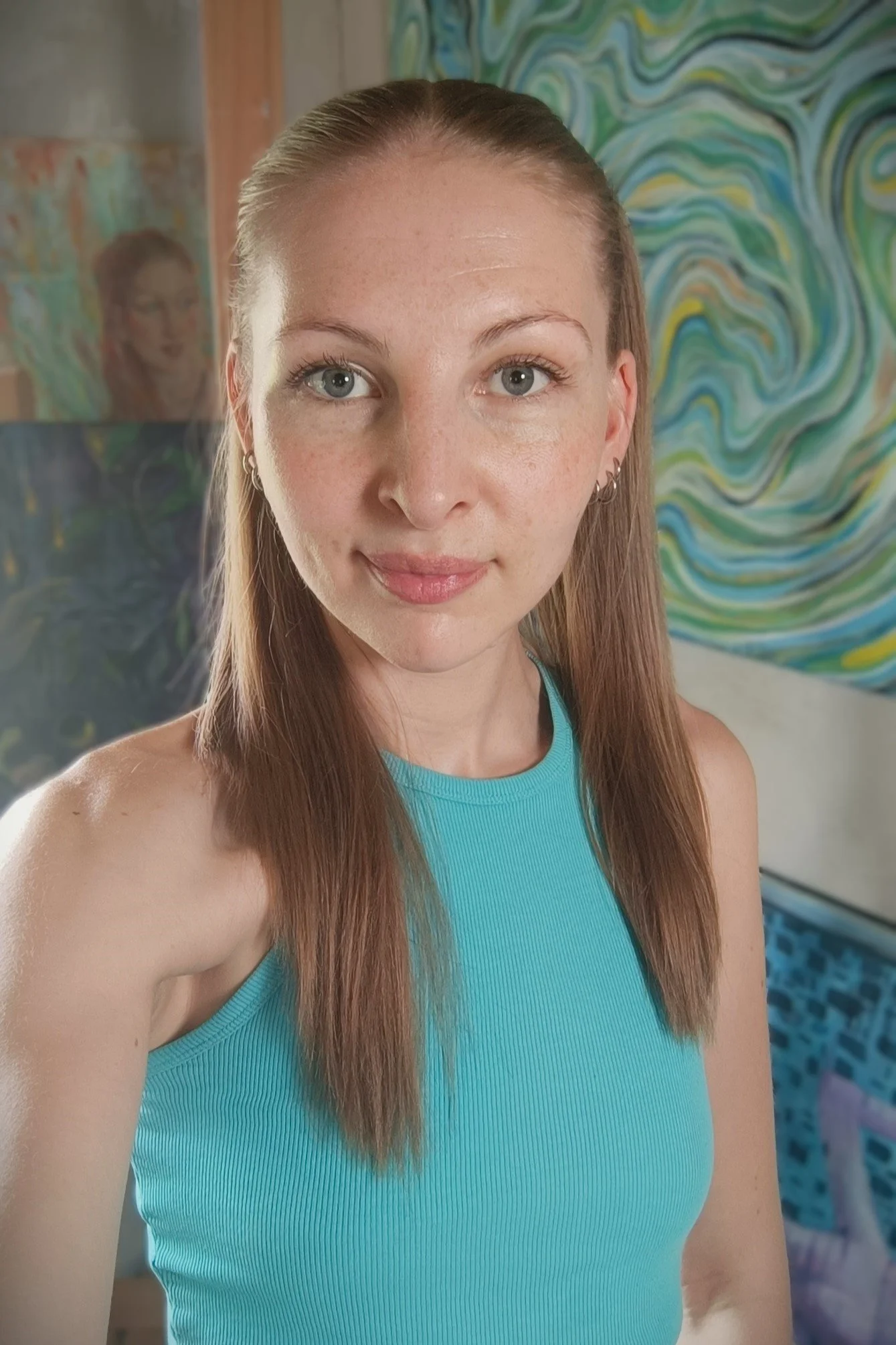Junge Frau in einem türkisblauen Oberteil nimmt Selfie vor einer bunten, abstrakten Wand