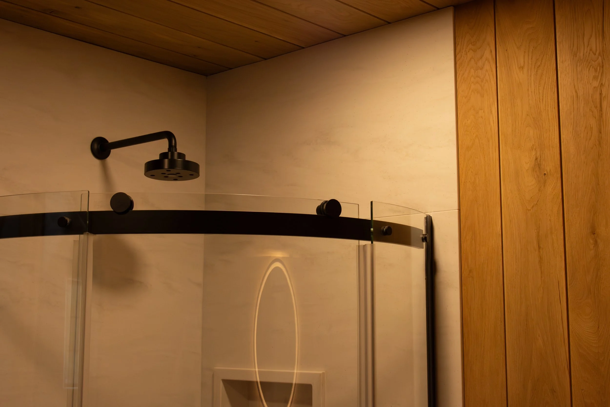 custom curved glass shower with tile panels and white oak surrounding it