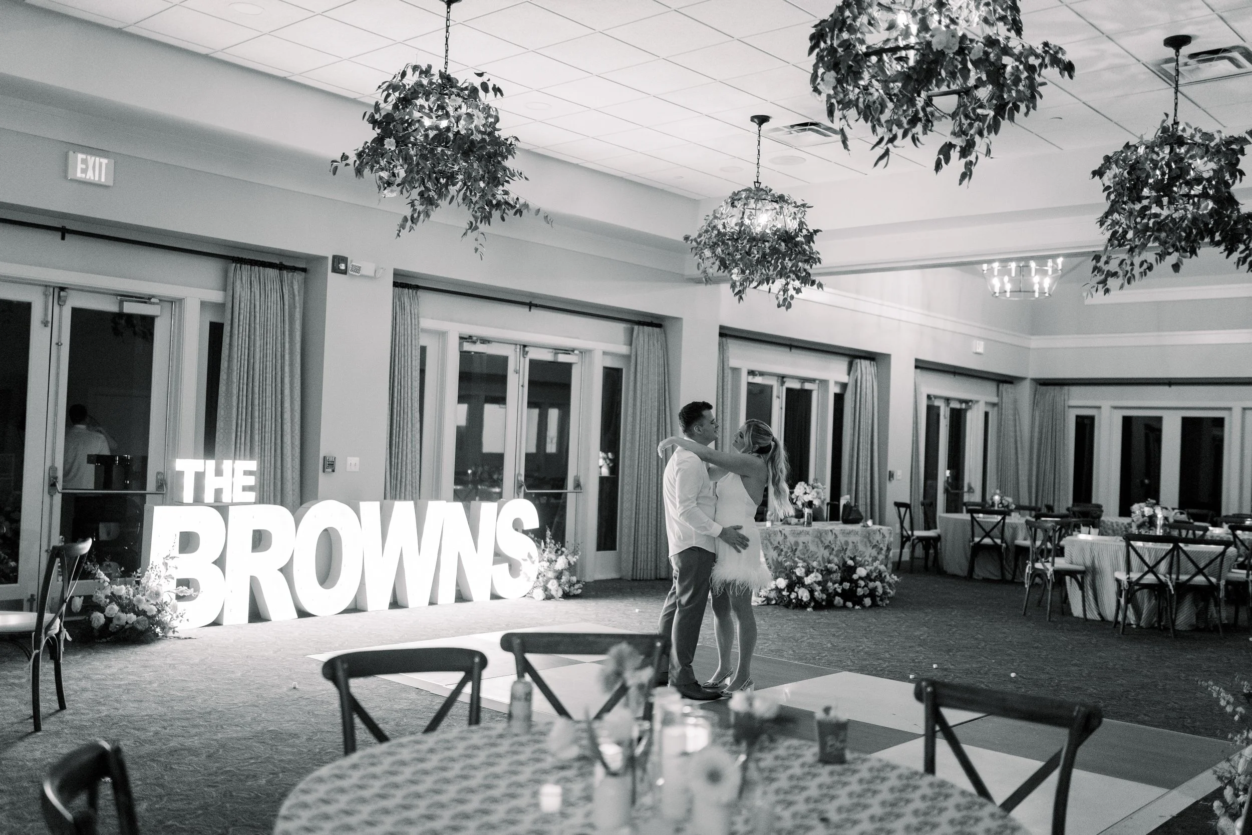 A couple dancing in a decorated banquet hall with floral arrangements, tables, and large signs that say 'THE BROWNS'.