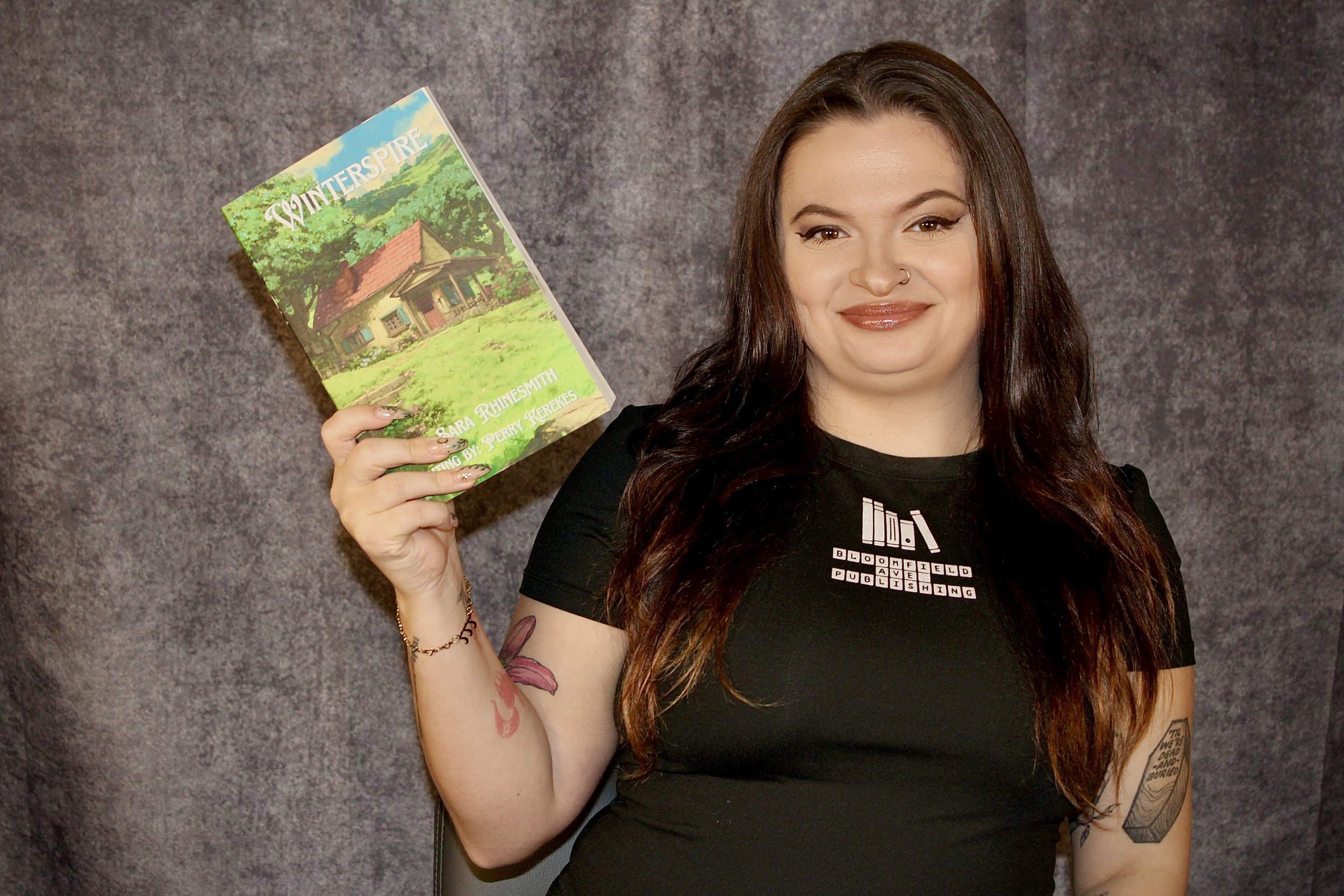 Author holding a book titled 'Winterspire' by Sara Rhinesmith
