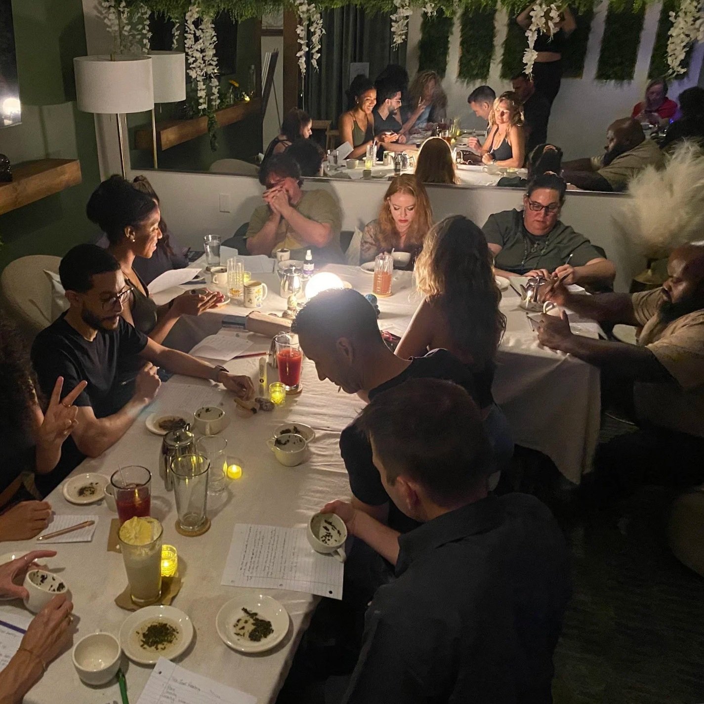 A group of people gathered around a dinner table enjoying a tea event at a low-lit, cozy alcohol free bar.