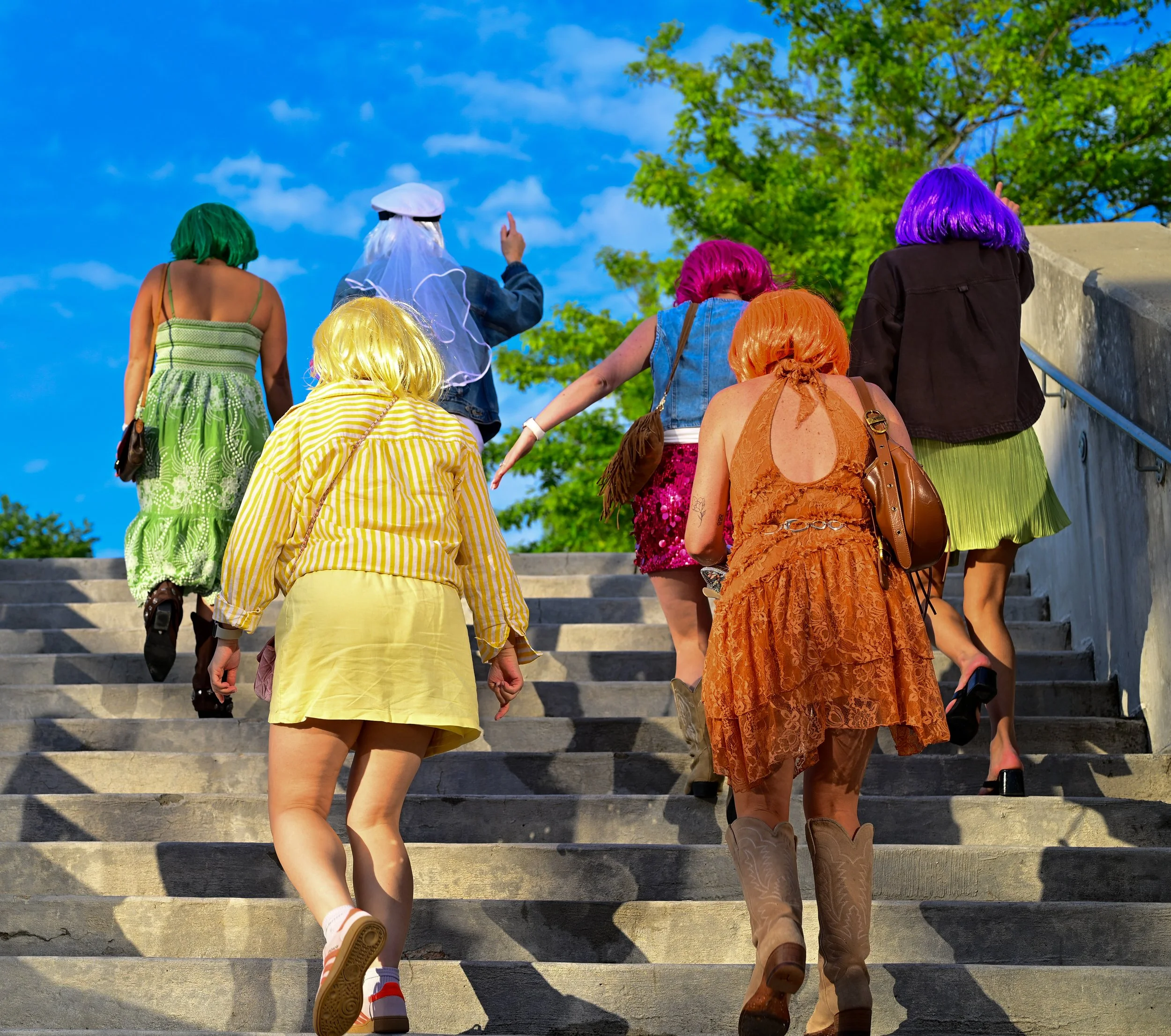 People dressed in colorful wigs and clothing walking up outdoor concrete stairs.