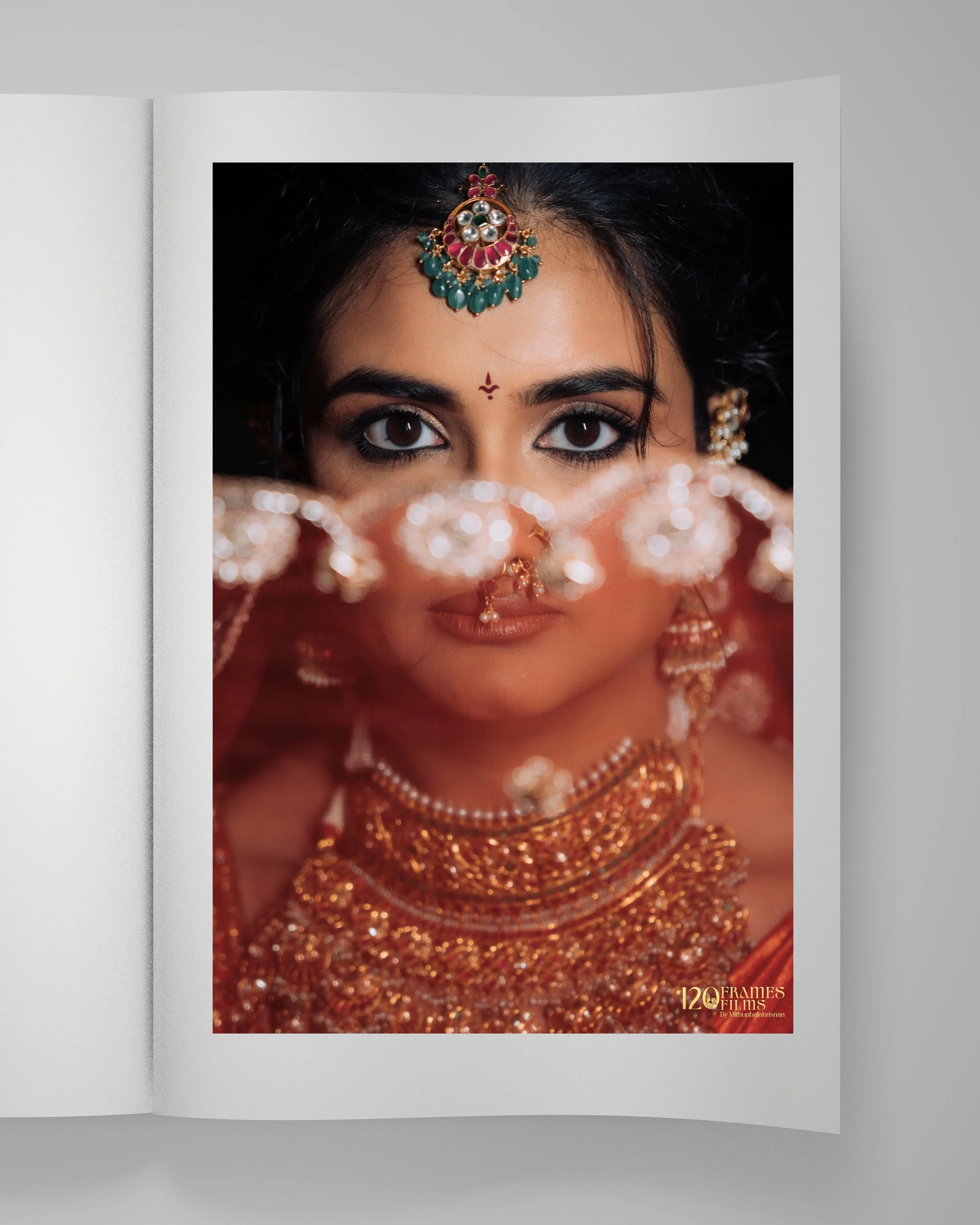 Close-up of an Indian bride with traditional gold jewelry, earrings, and a mang tikka on her forehead, partially covering her face with a red veil. The image showcases her expressive eyes and intricate jewelry details.