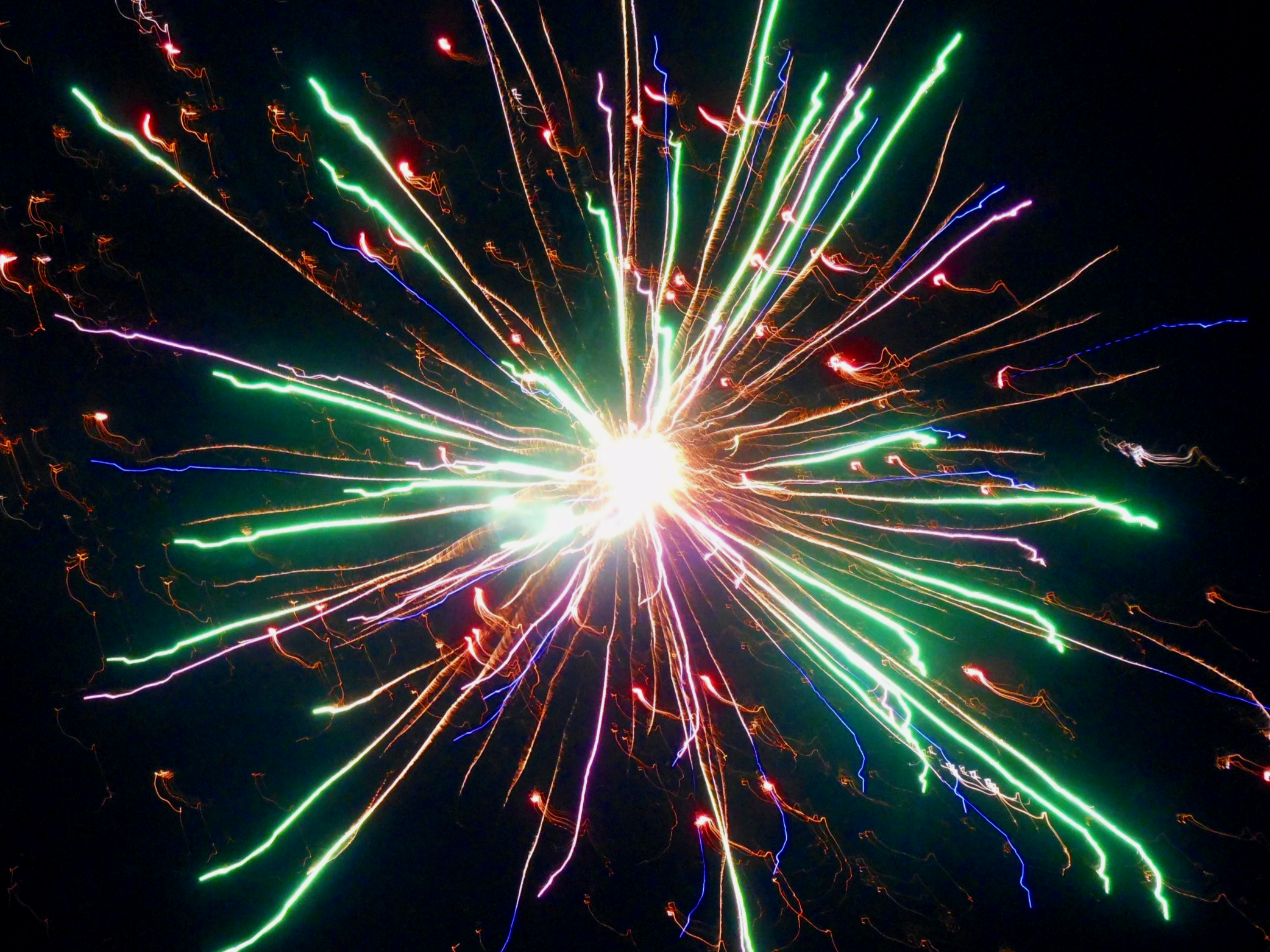 Colorful fireworks exploding against a dark sky with trails of red, green, purple, and orange light.