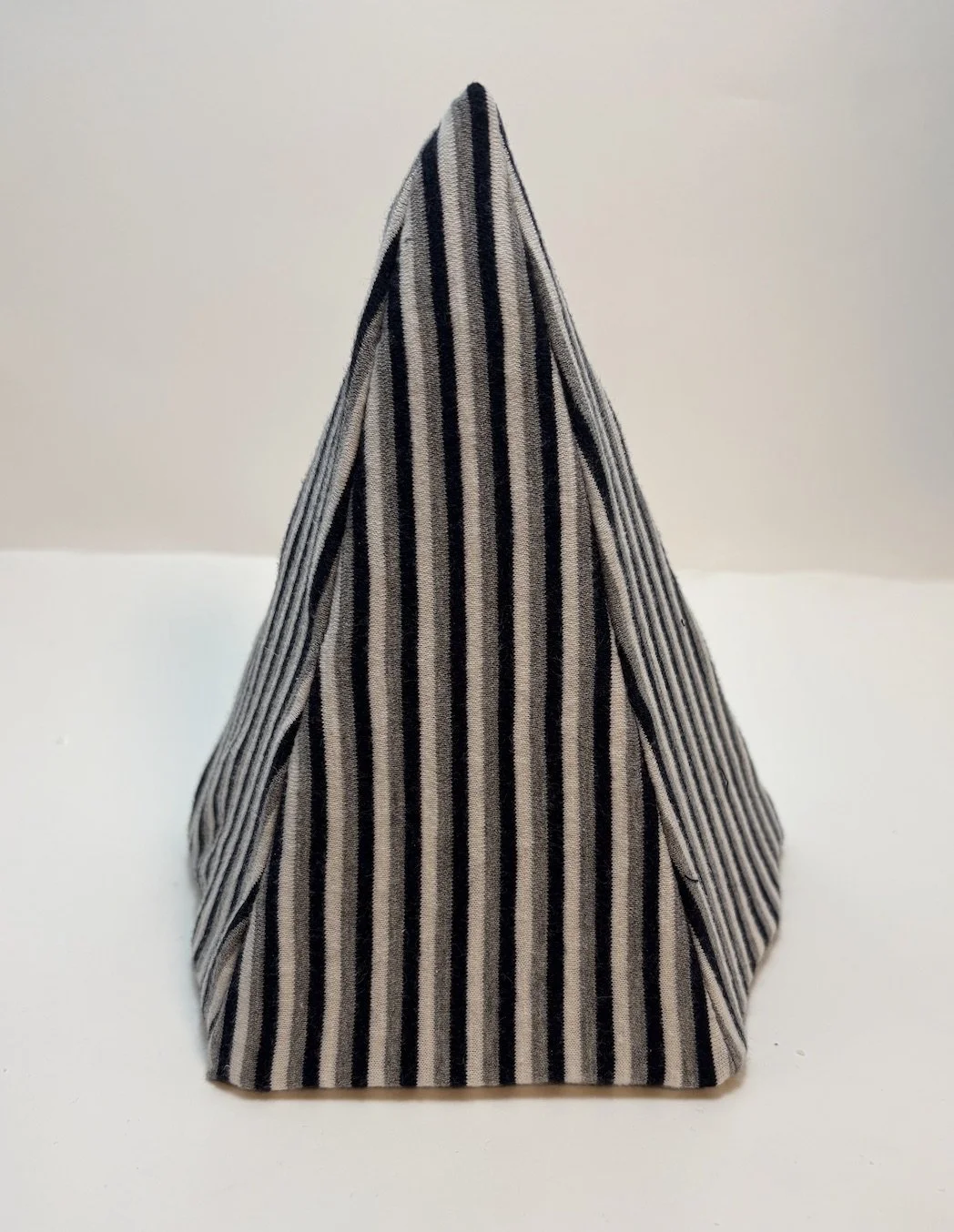 A cloth napkin with black and white vertical stripes folded into a cone shape on a white surface.