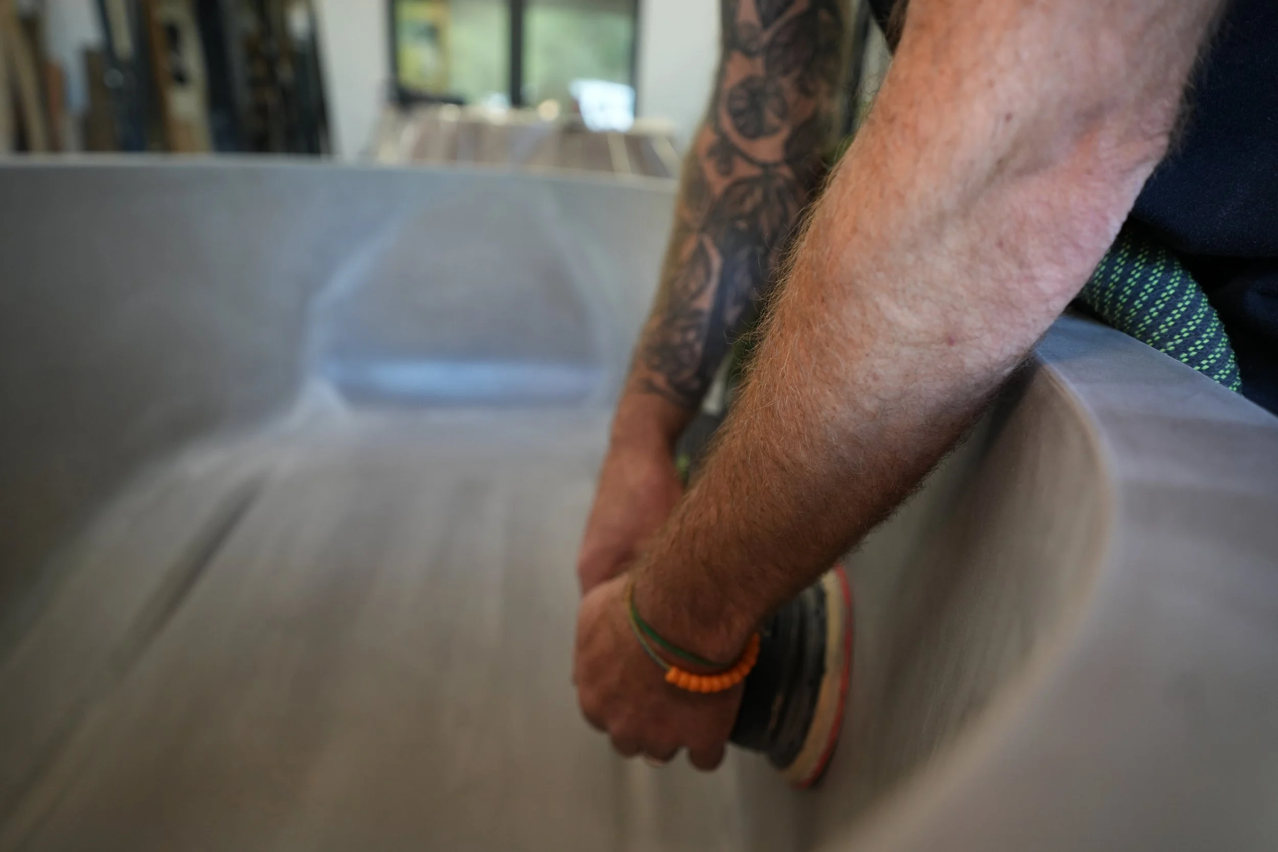 Close-up of a person's arm with tattoos, wearing a black shirt, resting on a table surface, with a background of a room with windows and furniture.