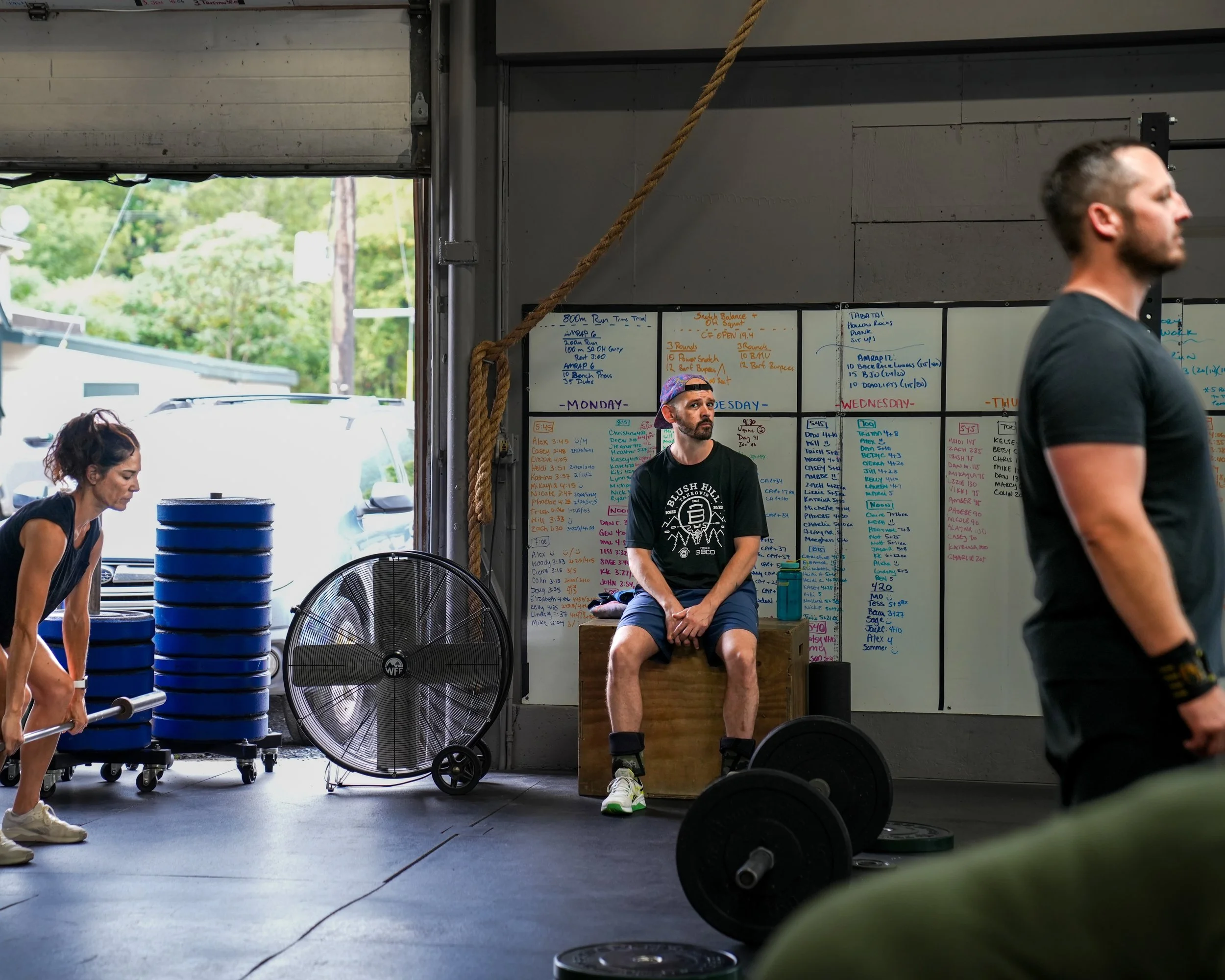 People in workout clothing near blackboard with workout schedule, weights, and punchy training environment.