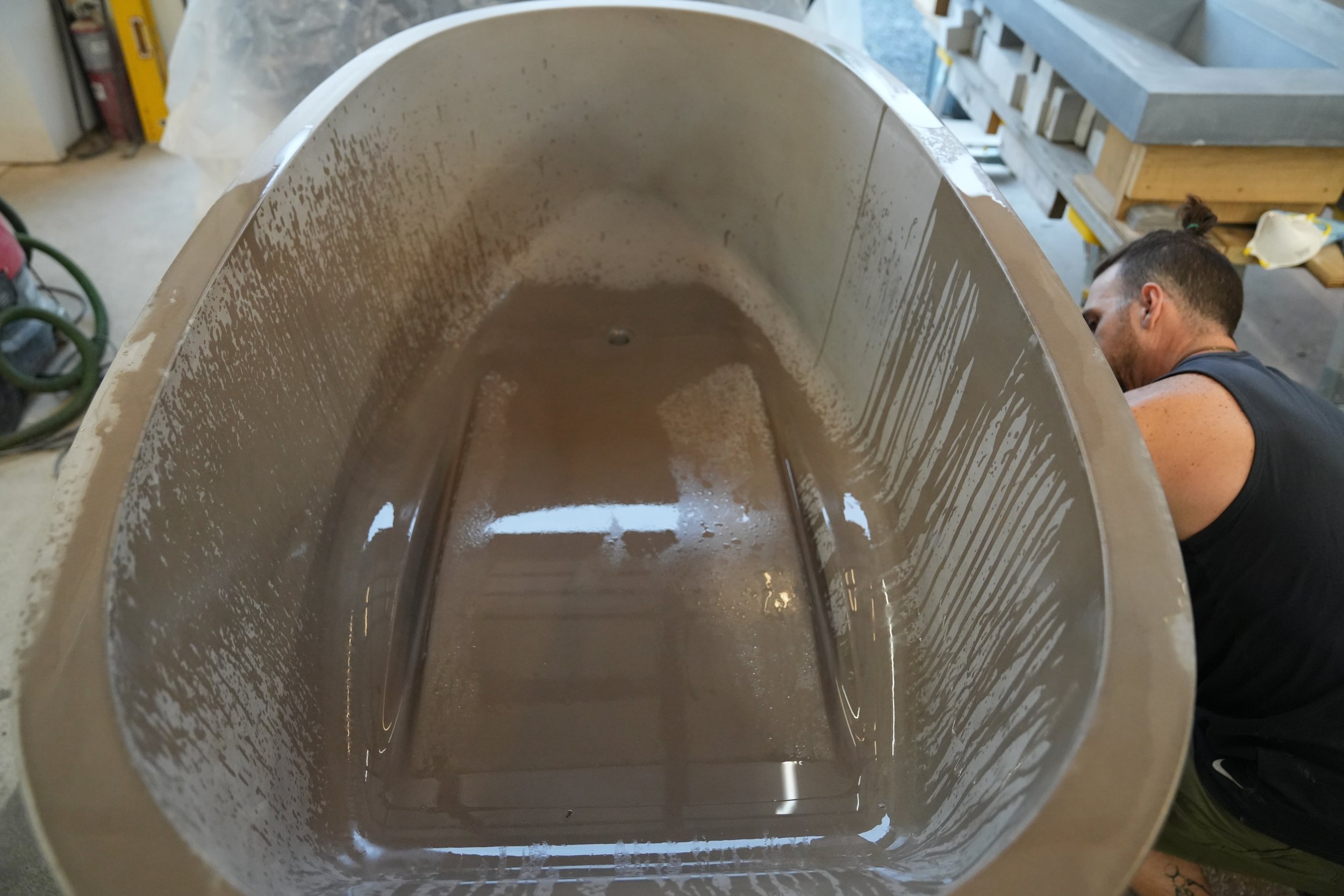 Close-up of the inside of a large, empty metal tank or vessel with a smooth, reflective inner surface, in a workshop or garage setting.