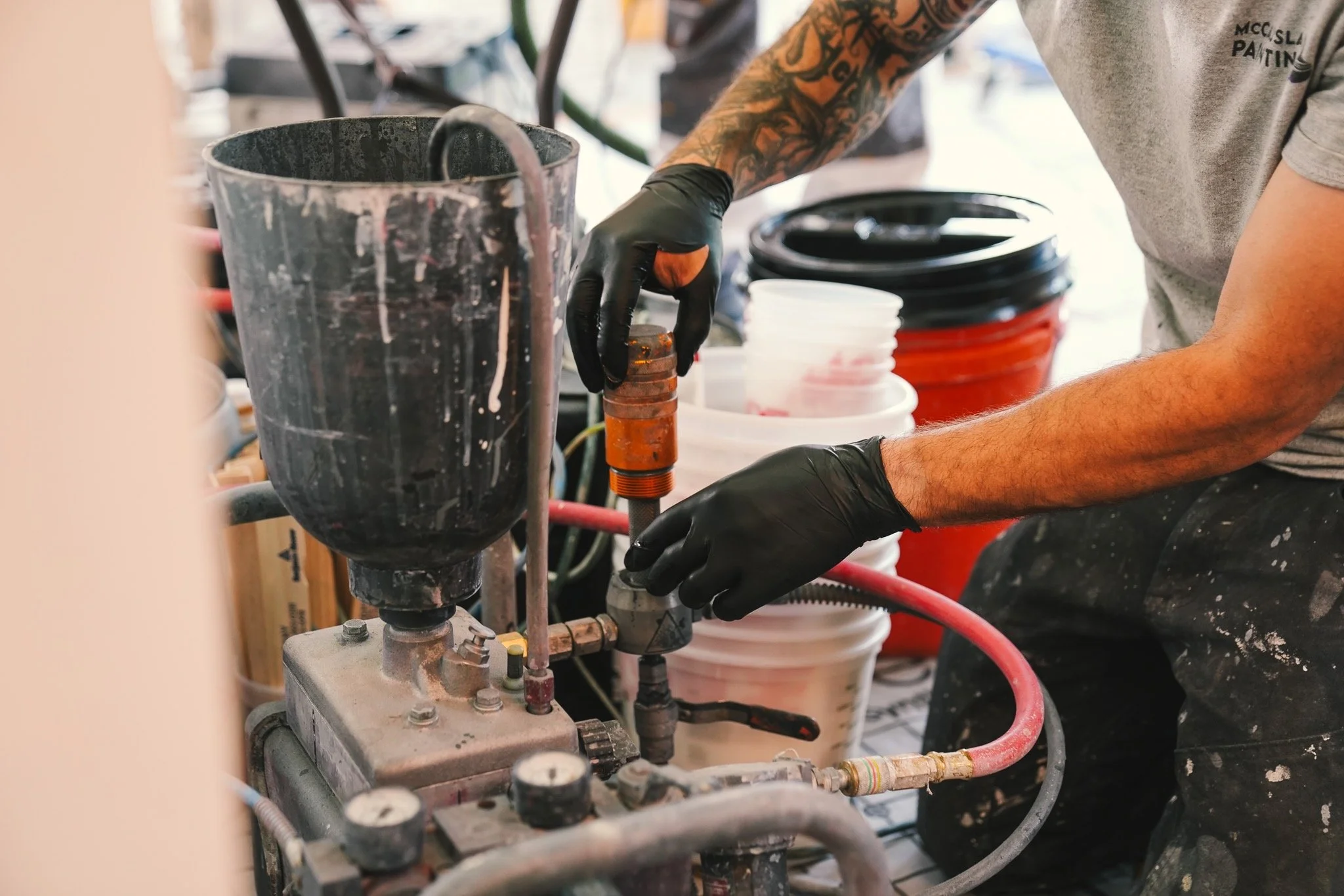 A person with tattoos and wearing black gloves working with plumbing or machinery connected to several buckets and pipes.
