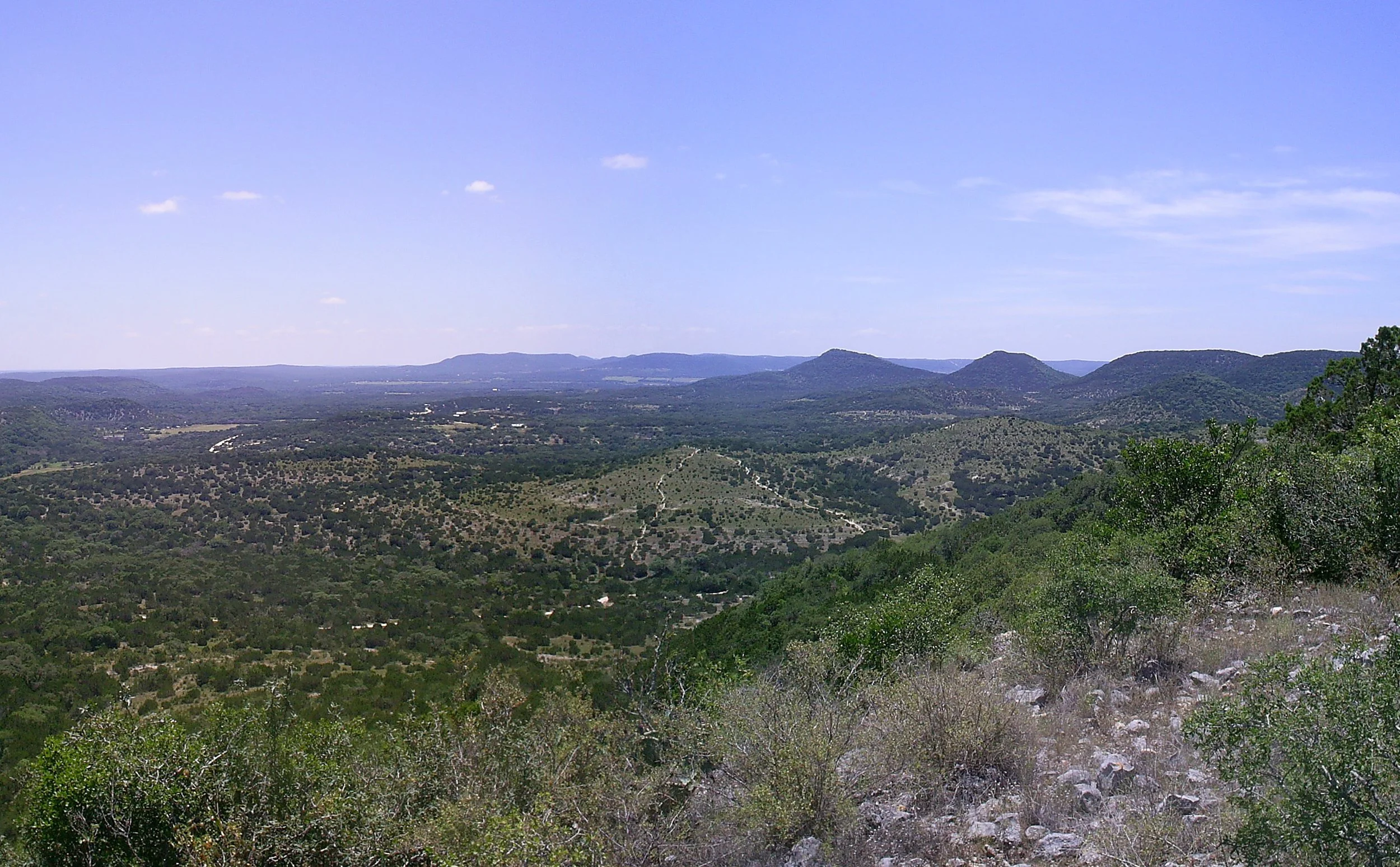 A scenic view of green rolling hills and mountains under a blue sky with a few scattered clouds.