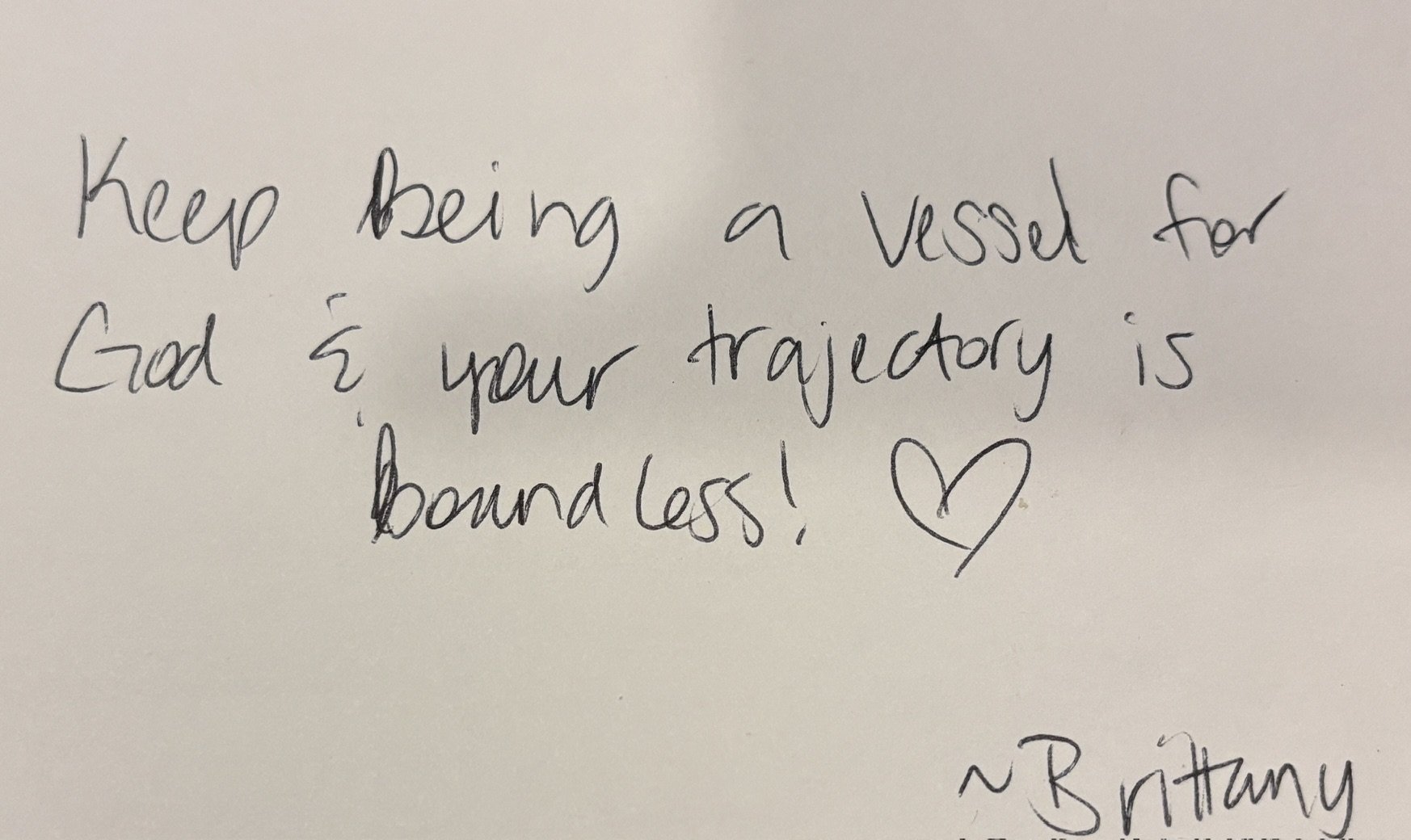 Handwritten note on white paper that says, 'Keep being a vessel for God & your trajectory is boundless!' with a small heart drawn at the end.