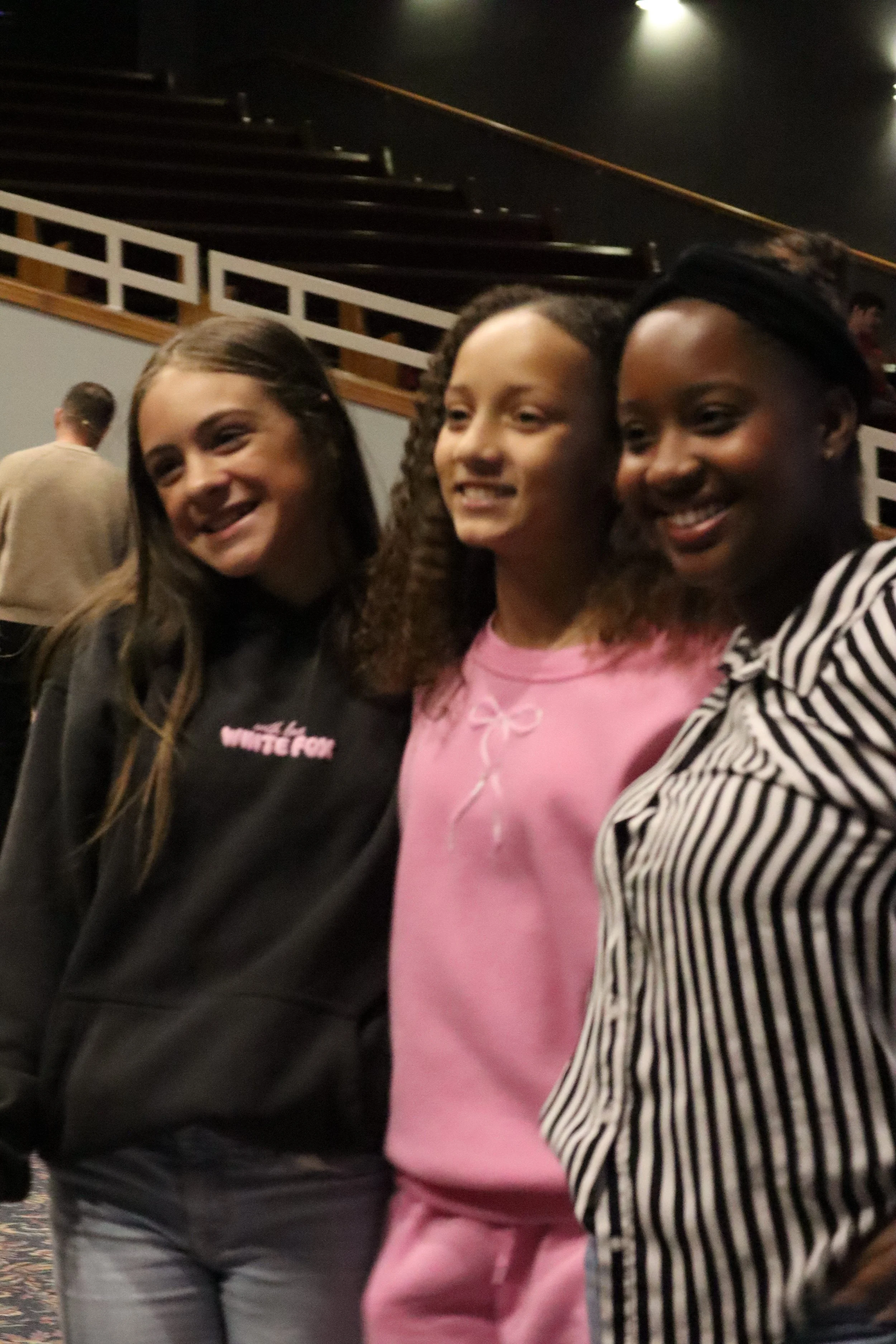 Three women taking a selfie together at an indoor event, smiling and posing for the camera.