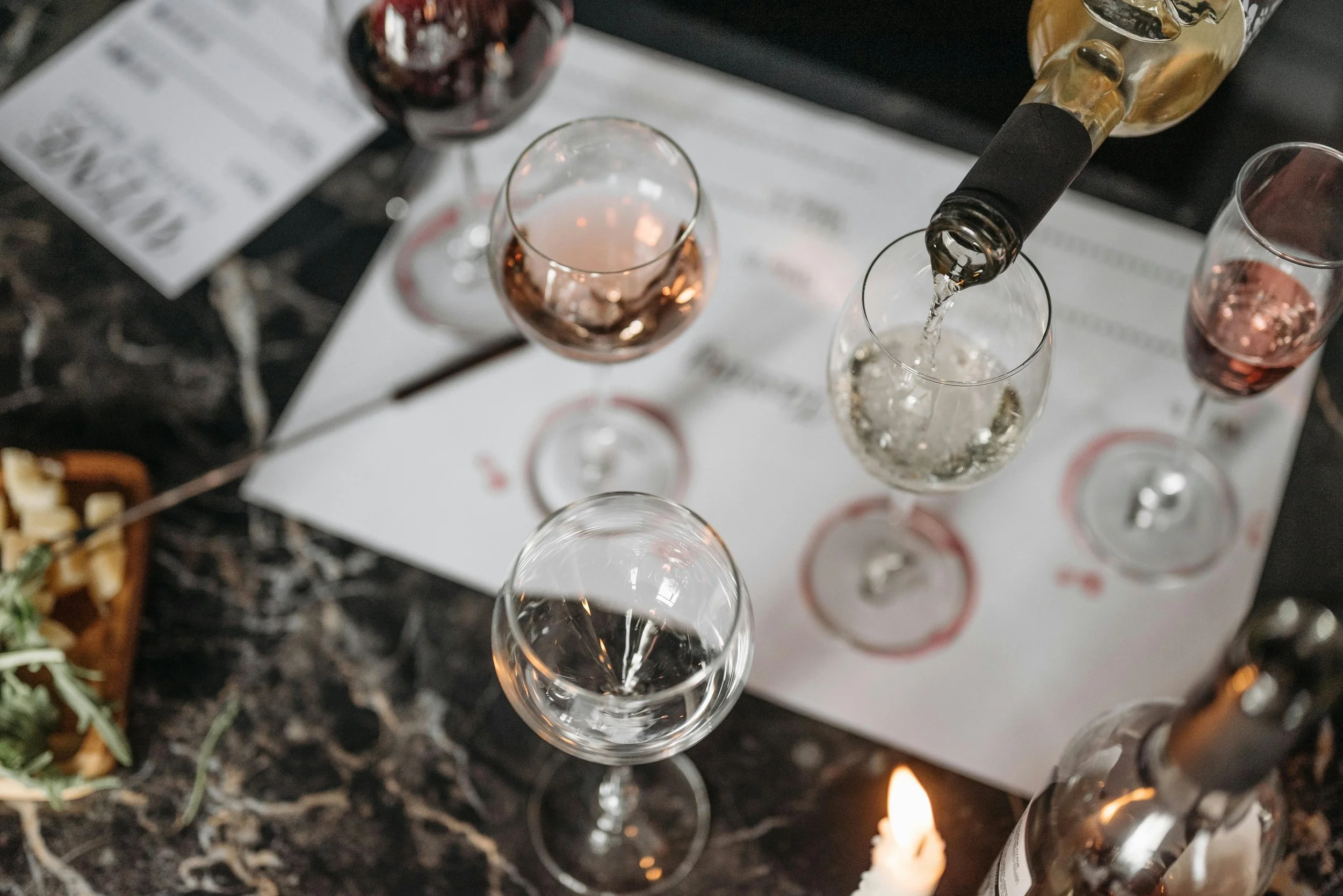 Overhead view of a wine tasting setup with white wine being poured and cheese nearby