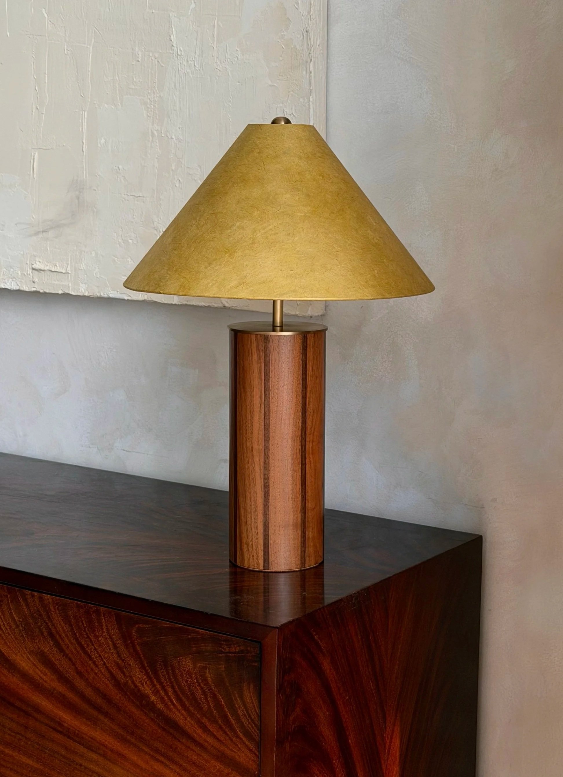A wooden table lamp with a green lampshade is placed on a dark wooden surface.