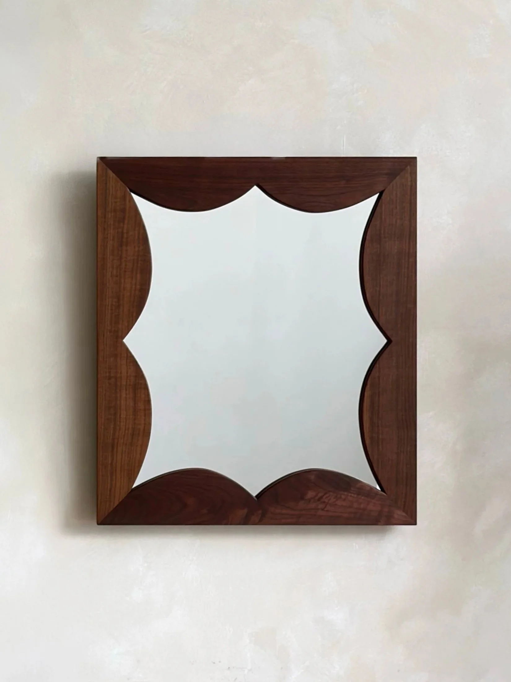 A wooden mirror with a decorative frame featuring curved cutouts, mounted on a white wall.