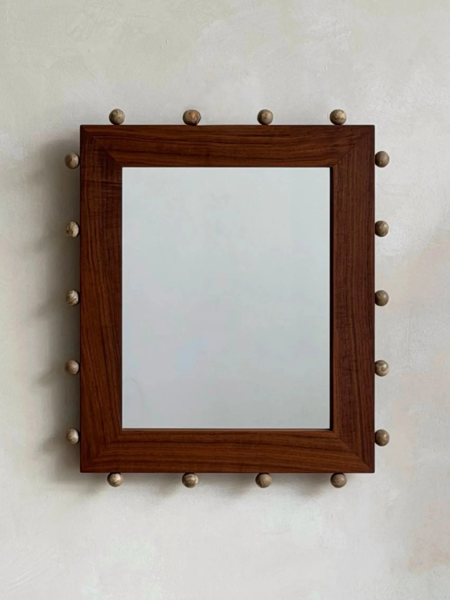 Wooden picture frame or mirror with rounddecorative ceramic accents around the border, mounted on a plain white wall.