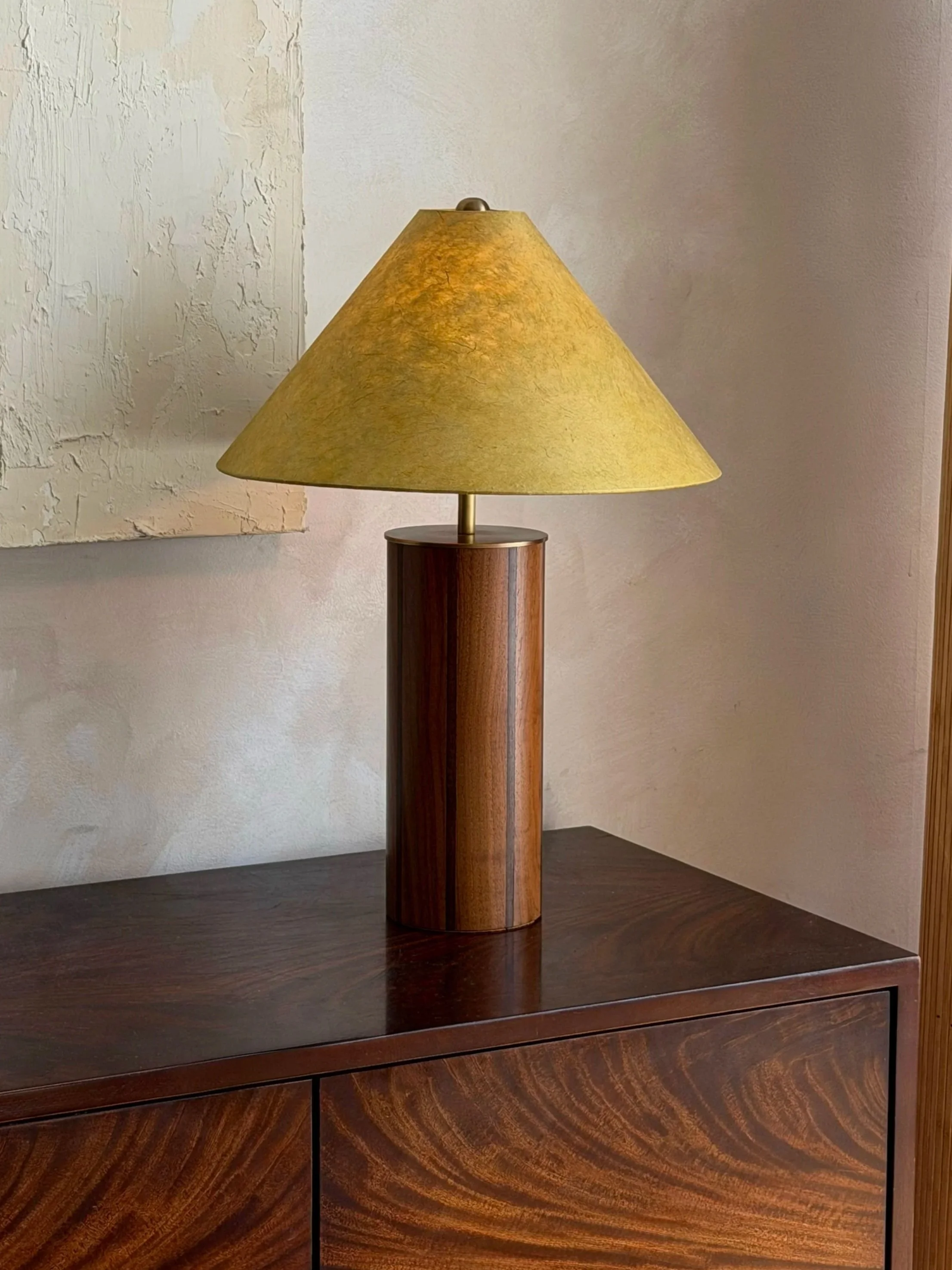 A wooden table lamp with a green lampshade placed on a dark wooden cabinet.