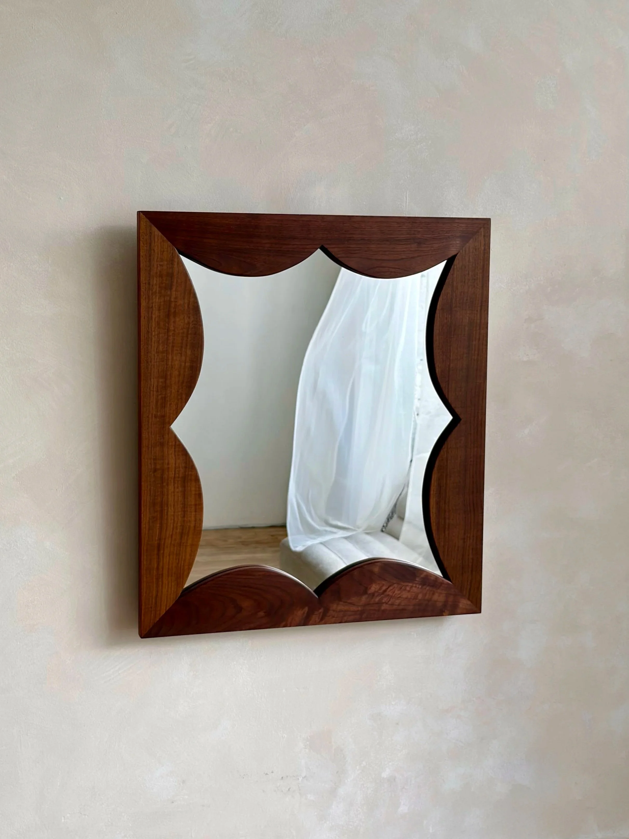 Wood-framed mirror with curved edges on a white wall.