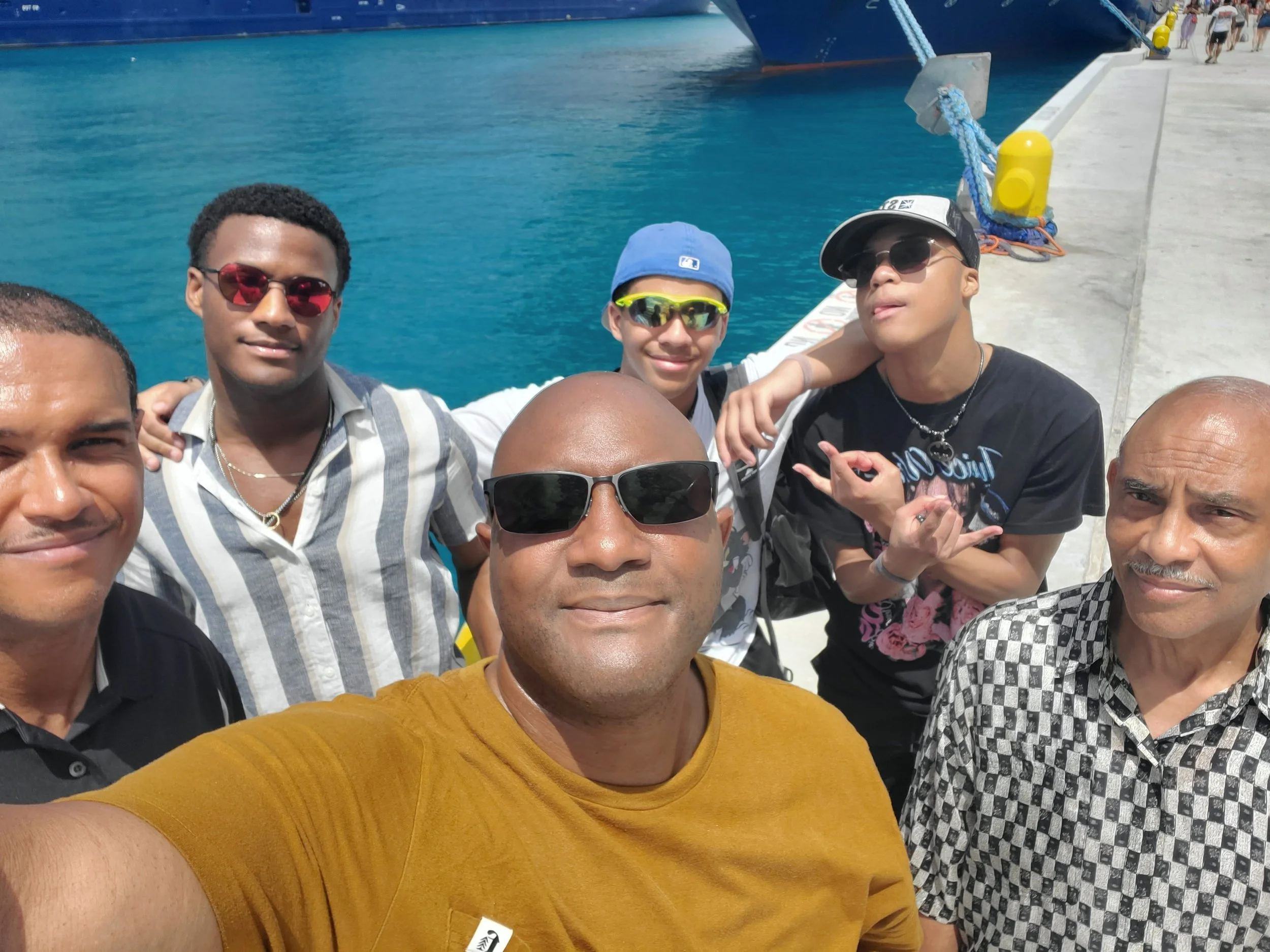 Group of people taking a selfie at the dock near the water, with boats in the background.