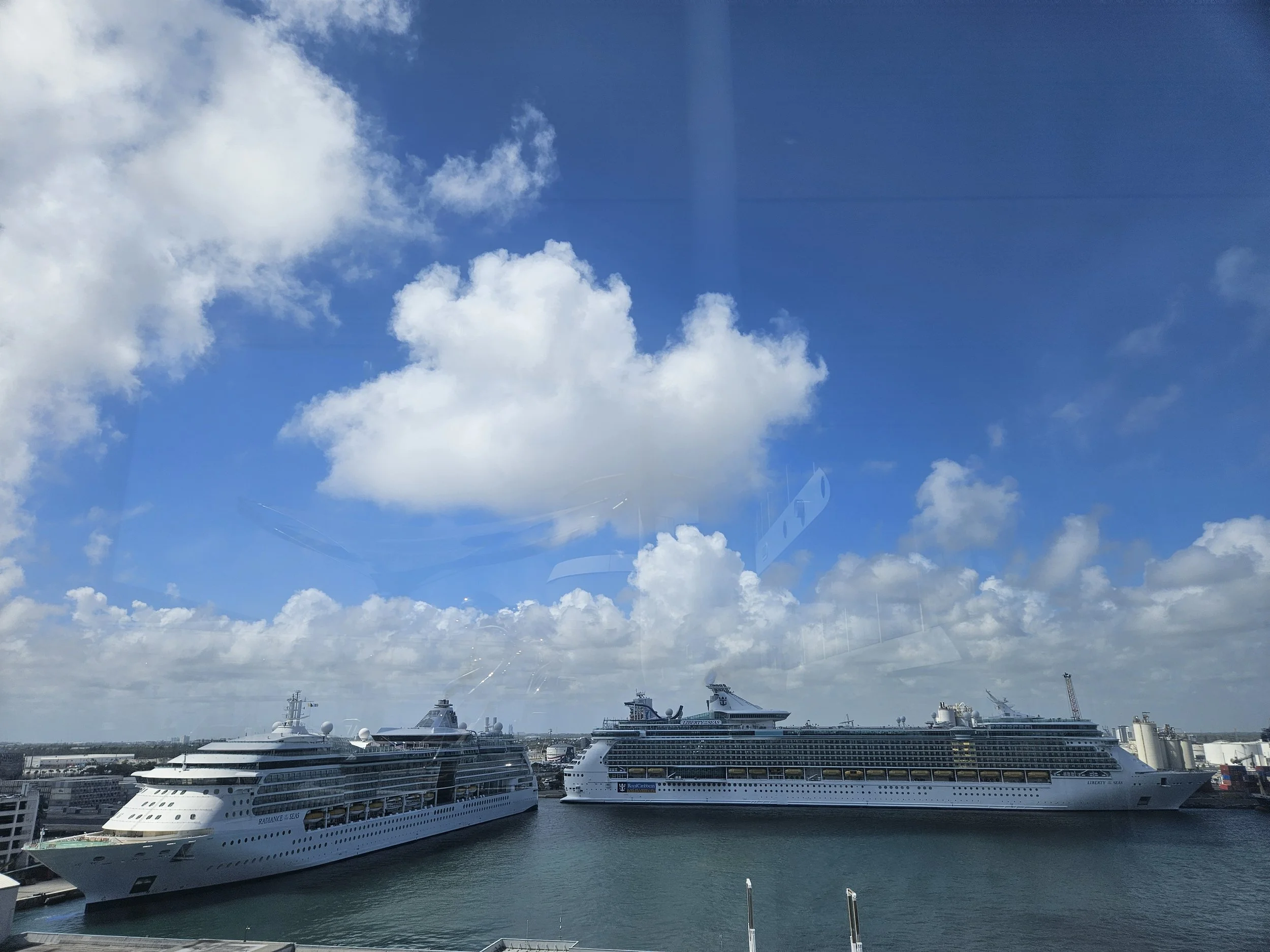 Several large white cruise ships docked at a port under a bright blue sky with scattered white clouds.