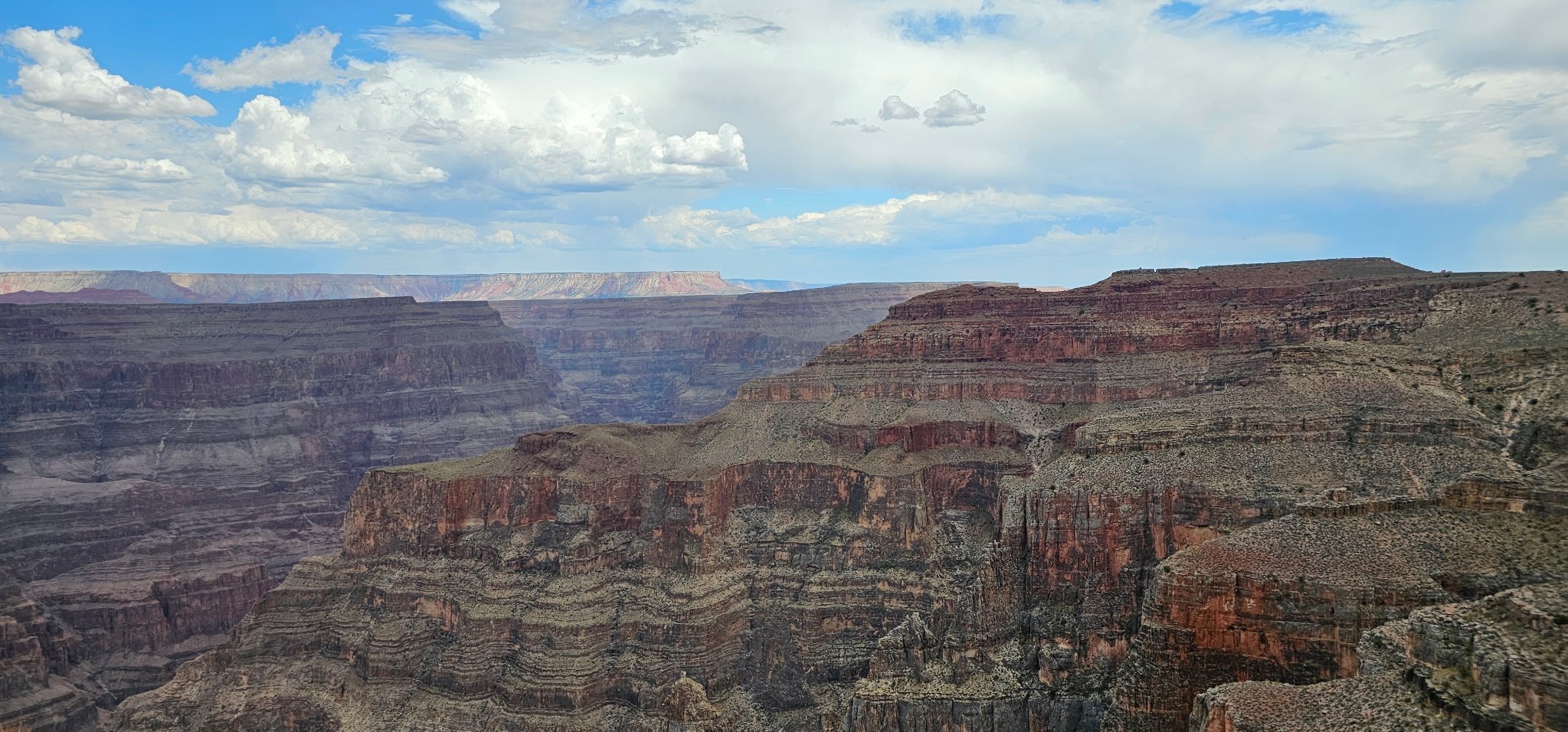 A panoramic view of the Grand Canyon showcasing layered red and brown rock formations under a partly cloudy sky.