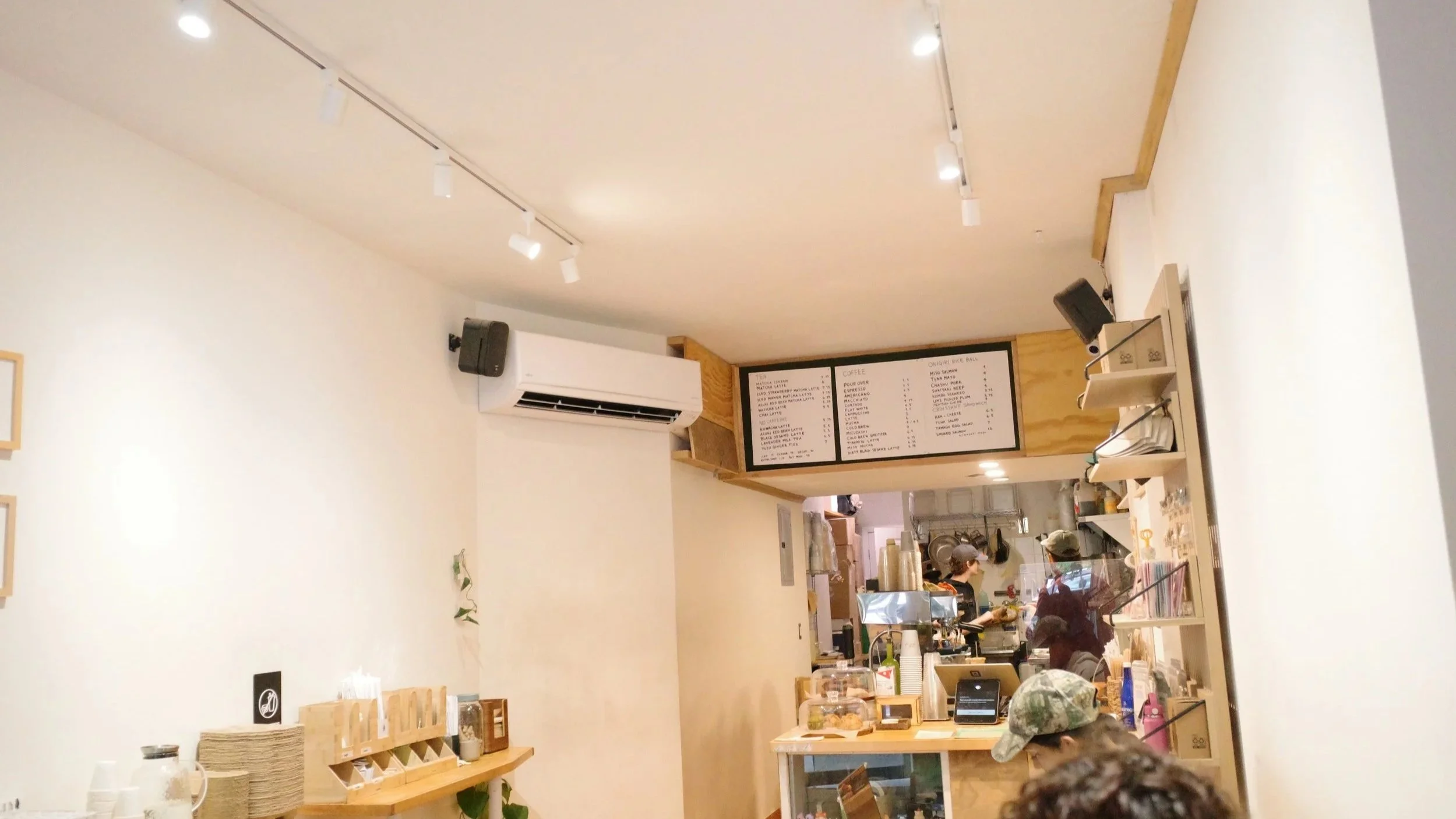 Interior of a cozy coffee shop with a wooden counter, menu boards, and staff preparing orders, visible through a glass display case.
