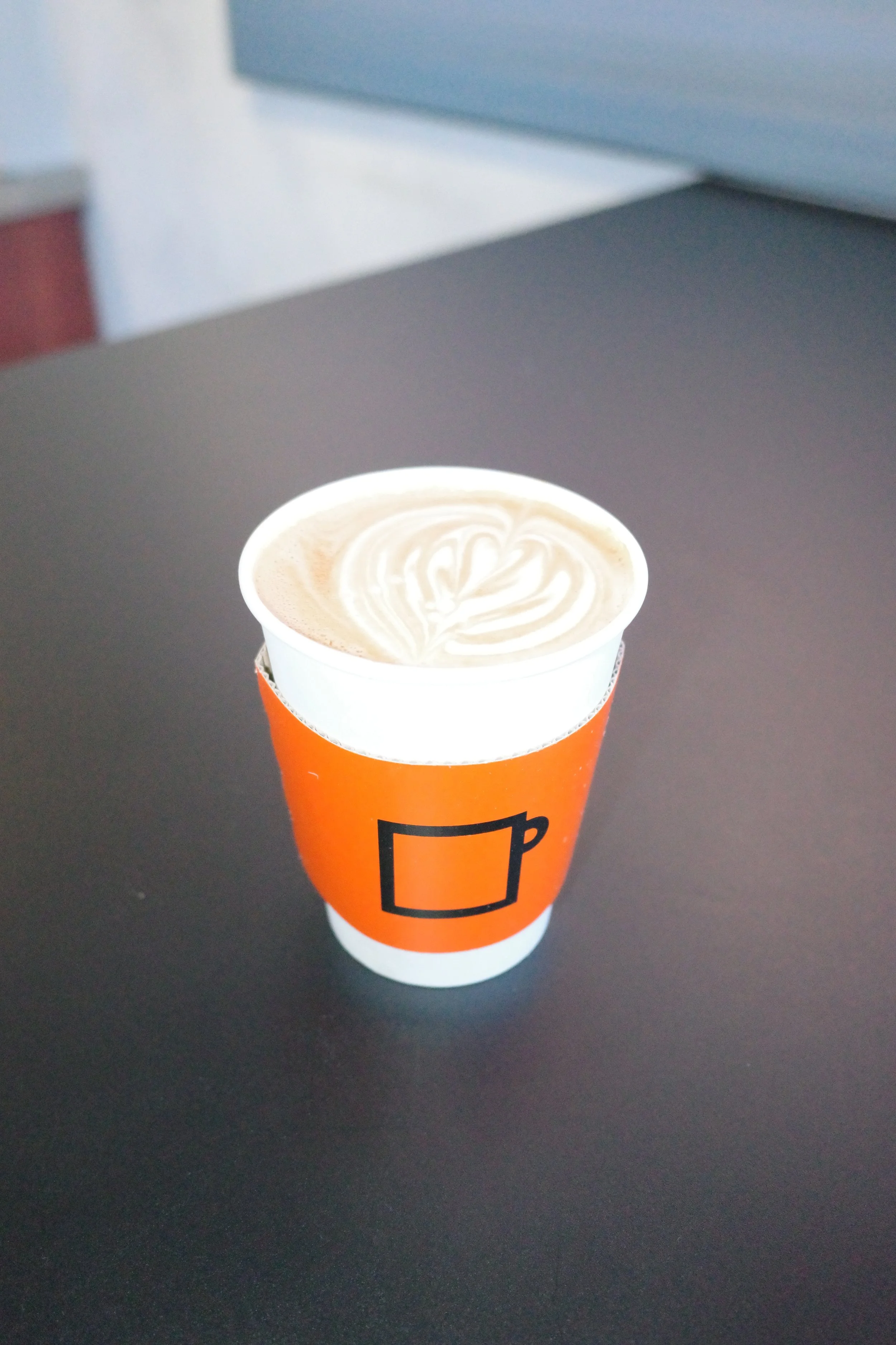 A disposable coffee cup with a latte topped with milk art, placed on a dark surface.