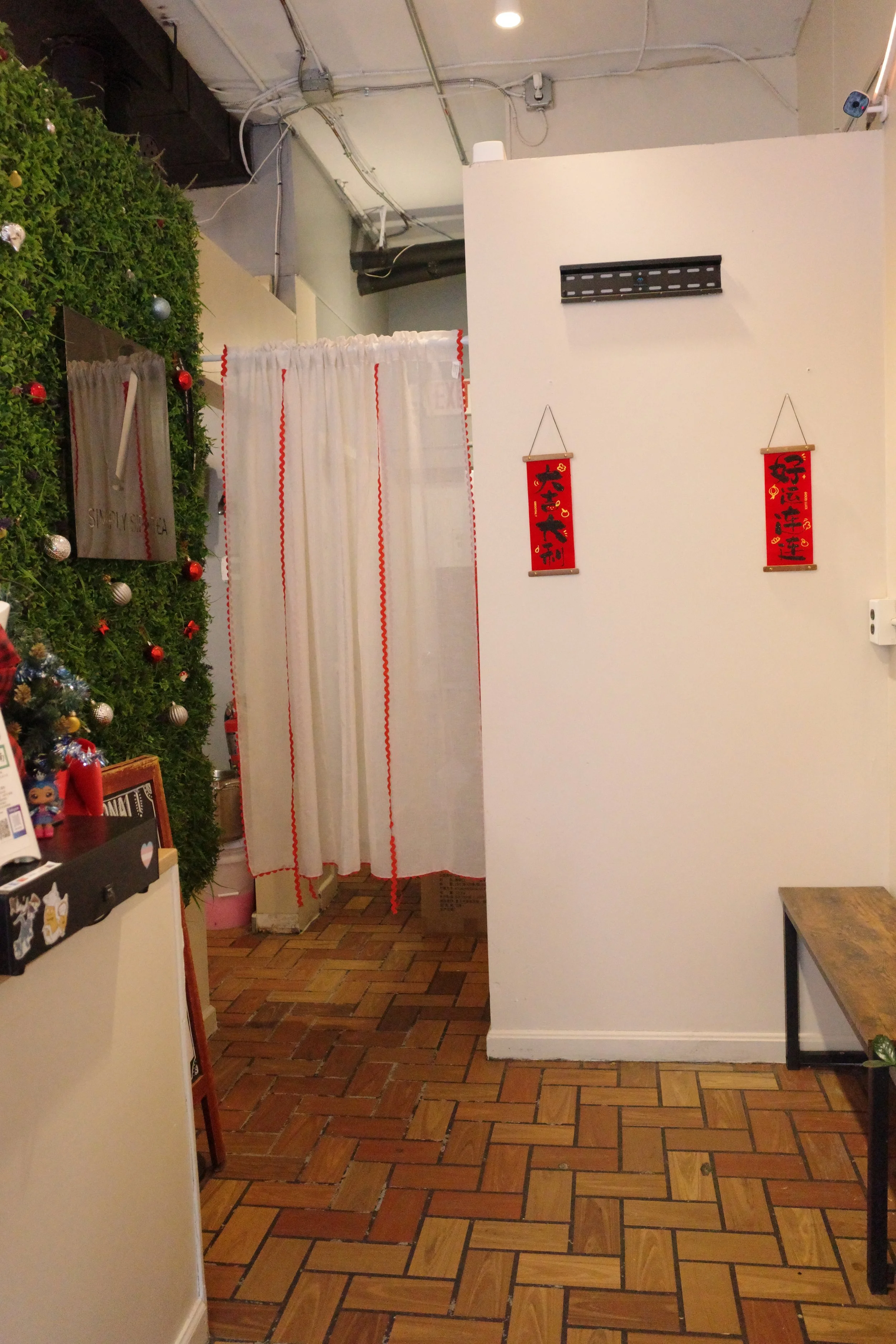 Interior of a room with a brick floor, a white wall with two Chinese New Year decorations, a curtain, and some Christmas decorations on a Christmas tree.