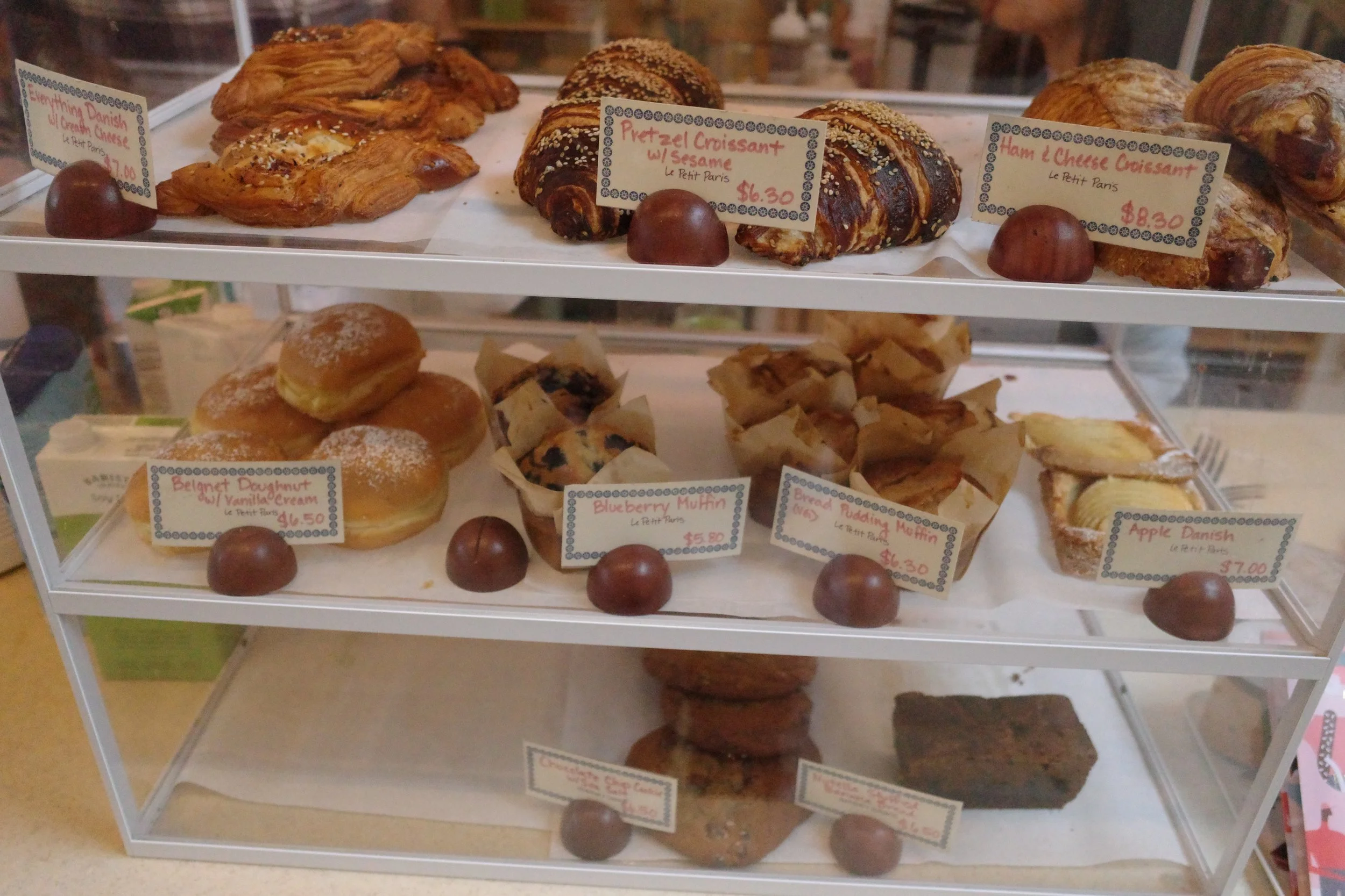 Display case with various Danish pastries and croissants, each labeled with names and prices, along with chocolate round balls.