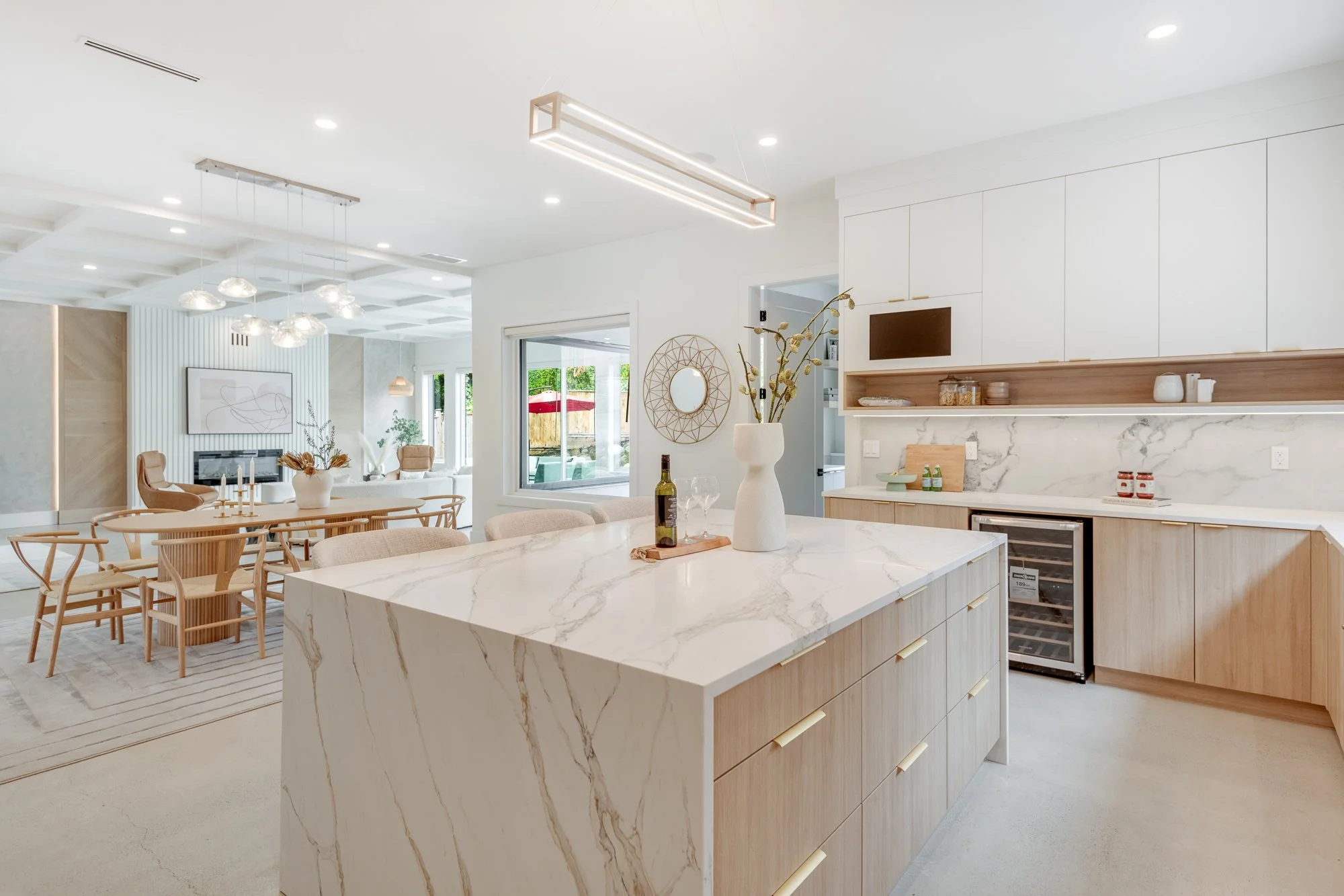Modern open-concept kitchen and dining area with white and light wood accents, marble countertops, and minimalist decor.