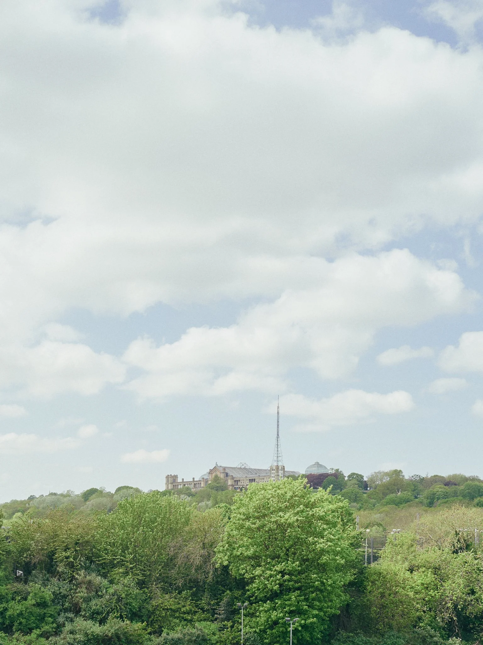 A large historic building with a tall radio tower on top, situated on a hill surrounded by lush green trees, under a cloudy sky.