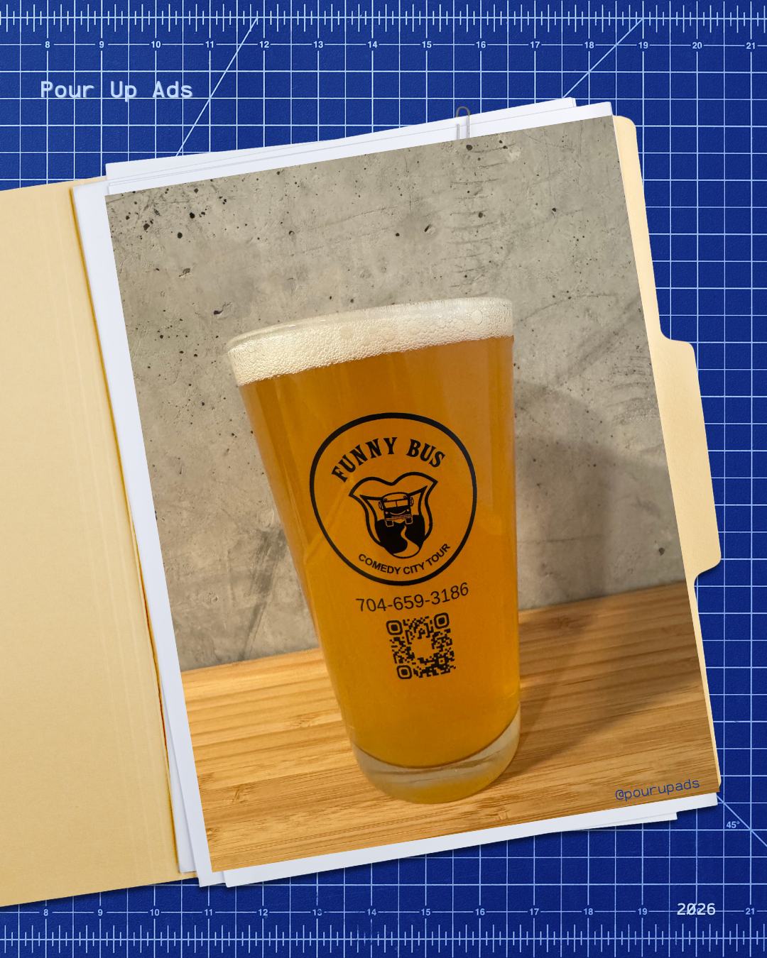 A pint of beer with a logo reading 'Funny Bus' and contact information, on a wooden surface against a concrete wall background.