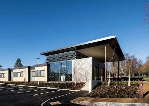 Exterior view of The Candover Clinic. Modern office building with large glass windows and a slanted roof, adjacent to a parking lot with marked spaces.