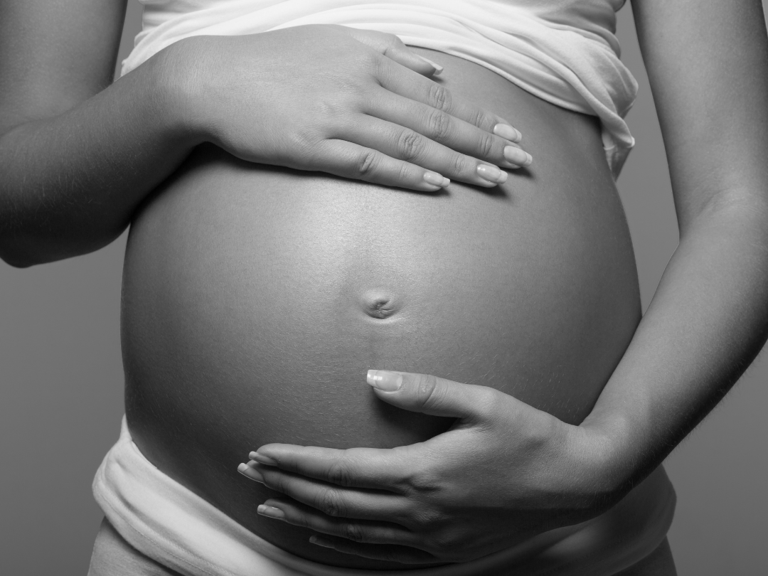 Black and white photograph of a pregnant woman with her hands gently cradling her belly.