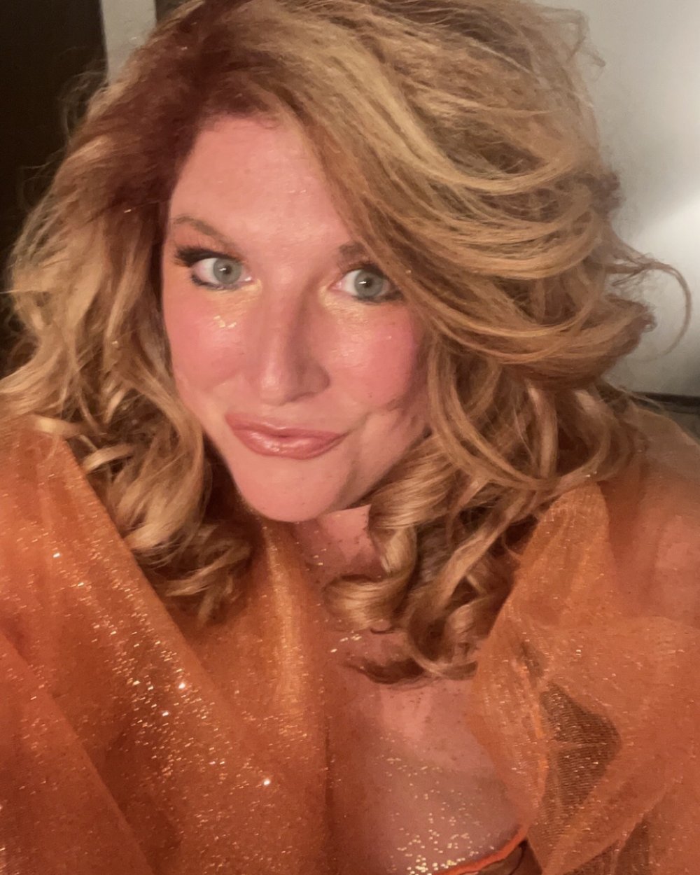 Carissa now with strawberry blonde curls, full glam makeup, wearing a sparkly orange dress — the result of the 25-product Amazon hair routin