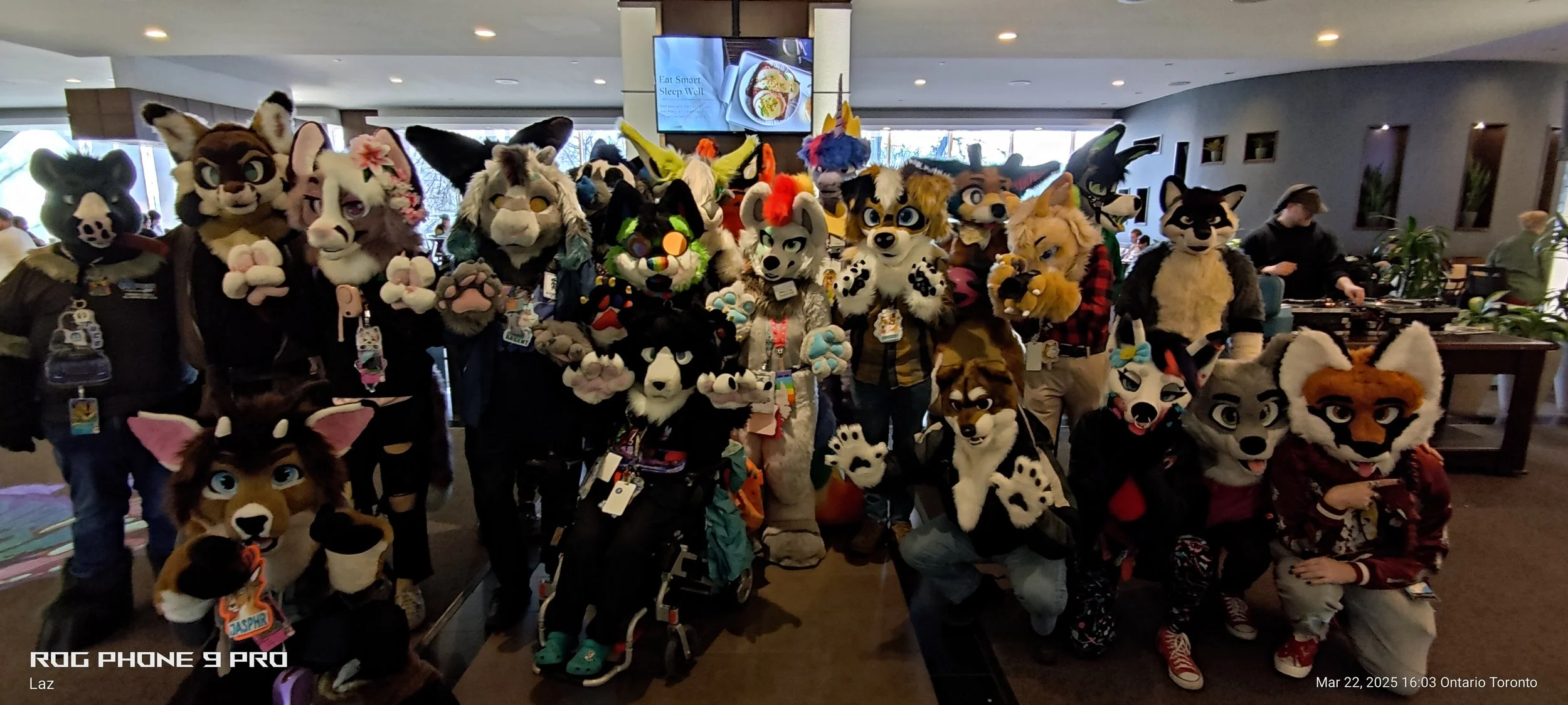 Group of people in elaborate animal costumes at an indoor furry convention, smiling and posing for a photo.