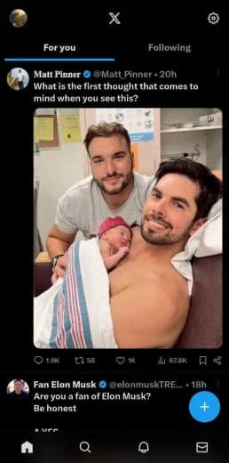 A man lying in a hospital bed holding a newborn baby, with another man standing beside him, all looking at the camera.