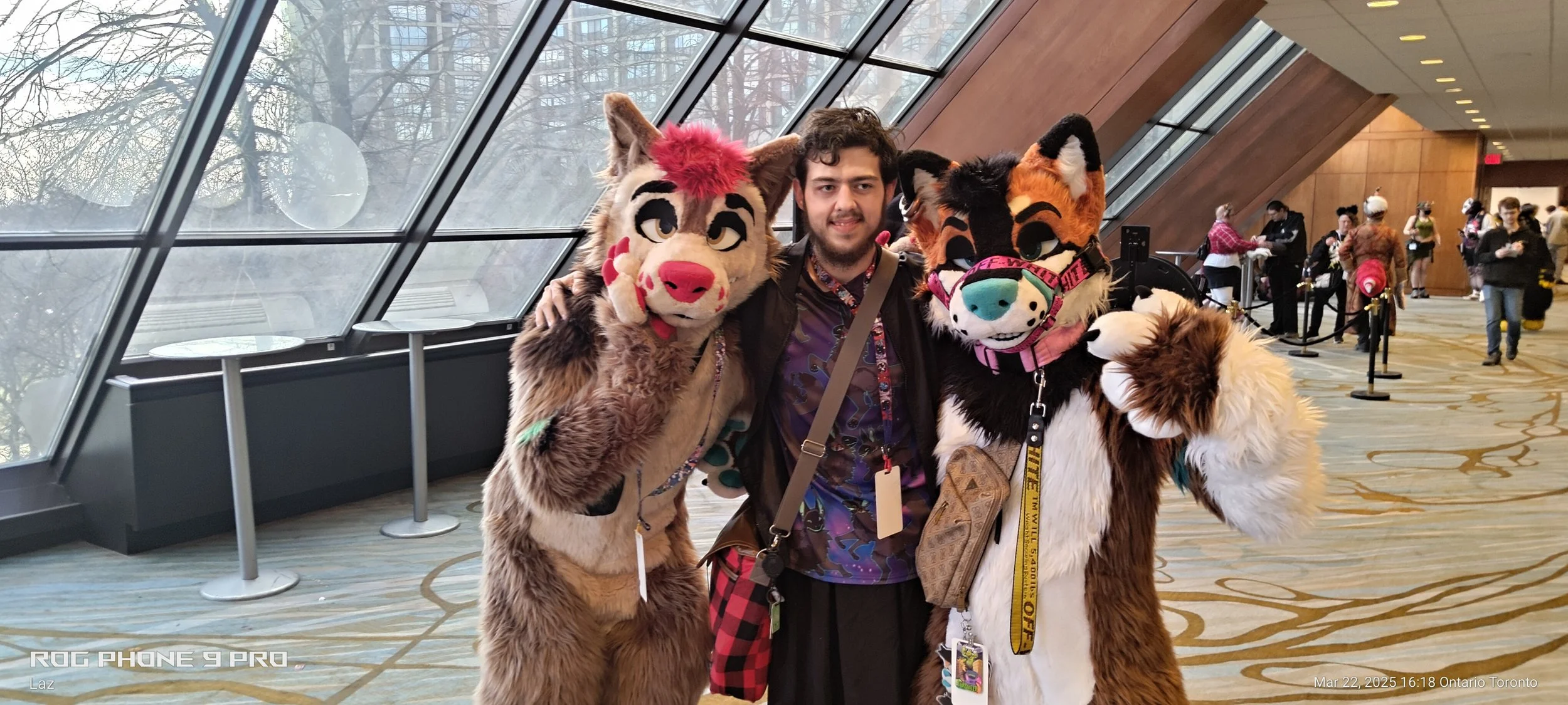 A man posing with two people dressed in furry animal costumes at an indoor convention center.