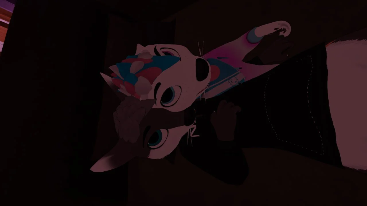 A person dressed in a black hoodie and black pants inside a dark room, holding a cat costume mask with a colorful, patterned design, and pointing a finger at the camera.