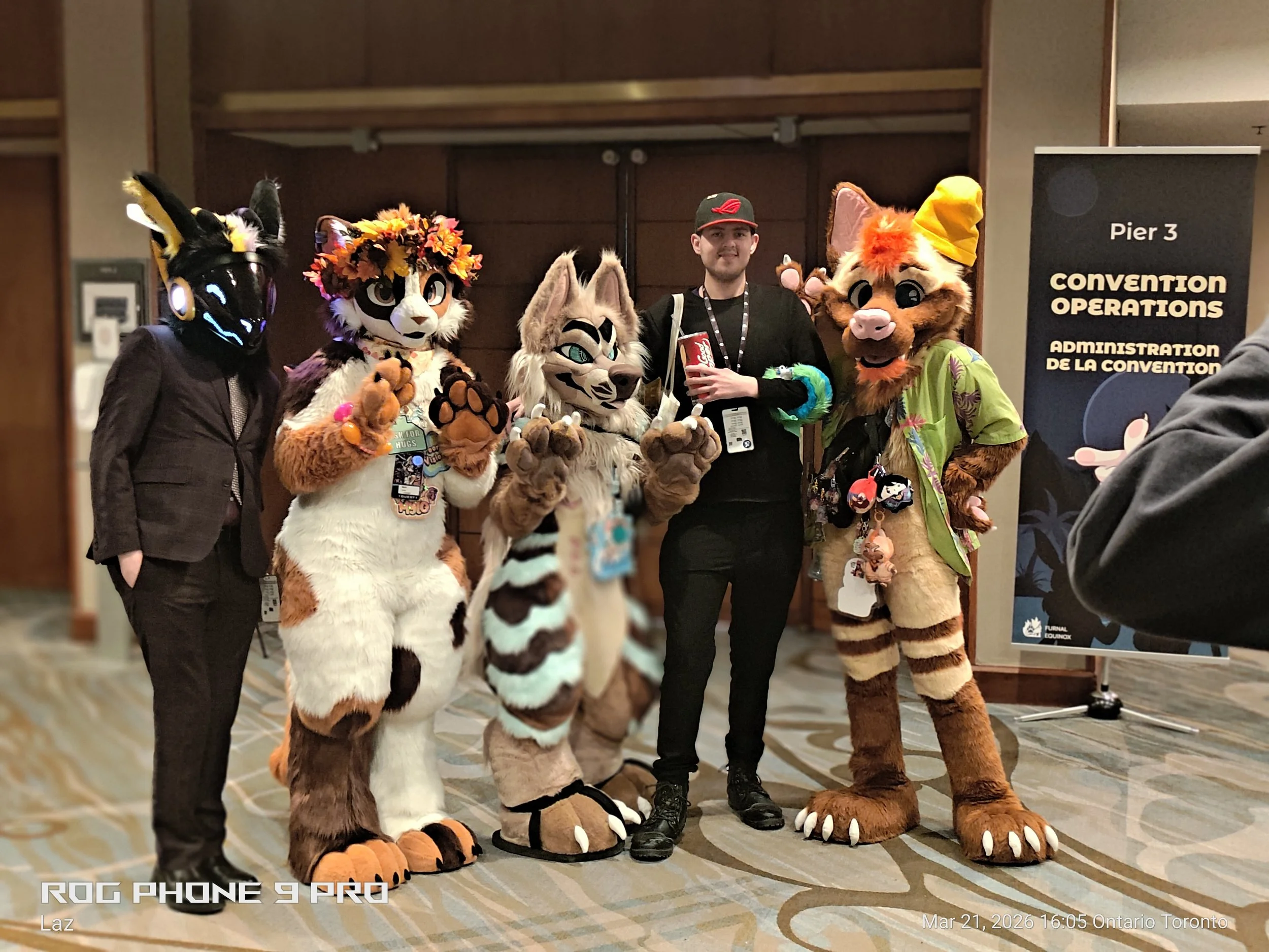 A group of people in animal costumes and a person in casual clothing at a convention, standing in a line with a sign indicating 'Pier 3 Convention Operations'.