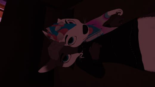 A person dressed in a colorful costume with a large animal mask, possibly a fox or wolf, holding a puppet or stuffed animal in a dimly lit room.