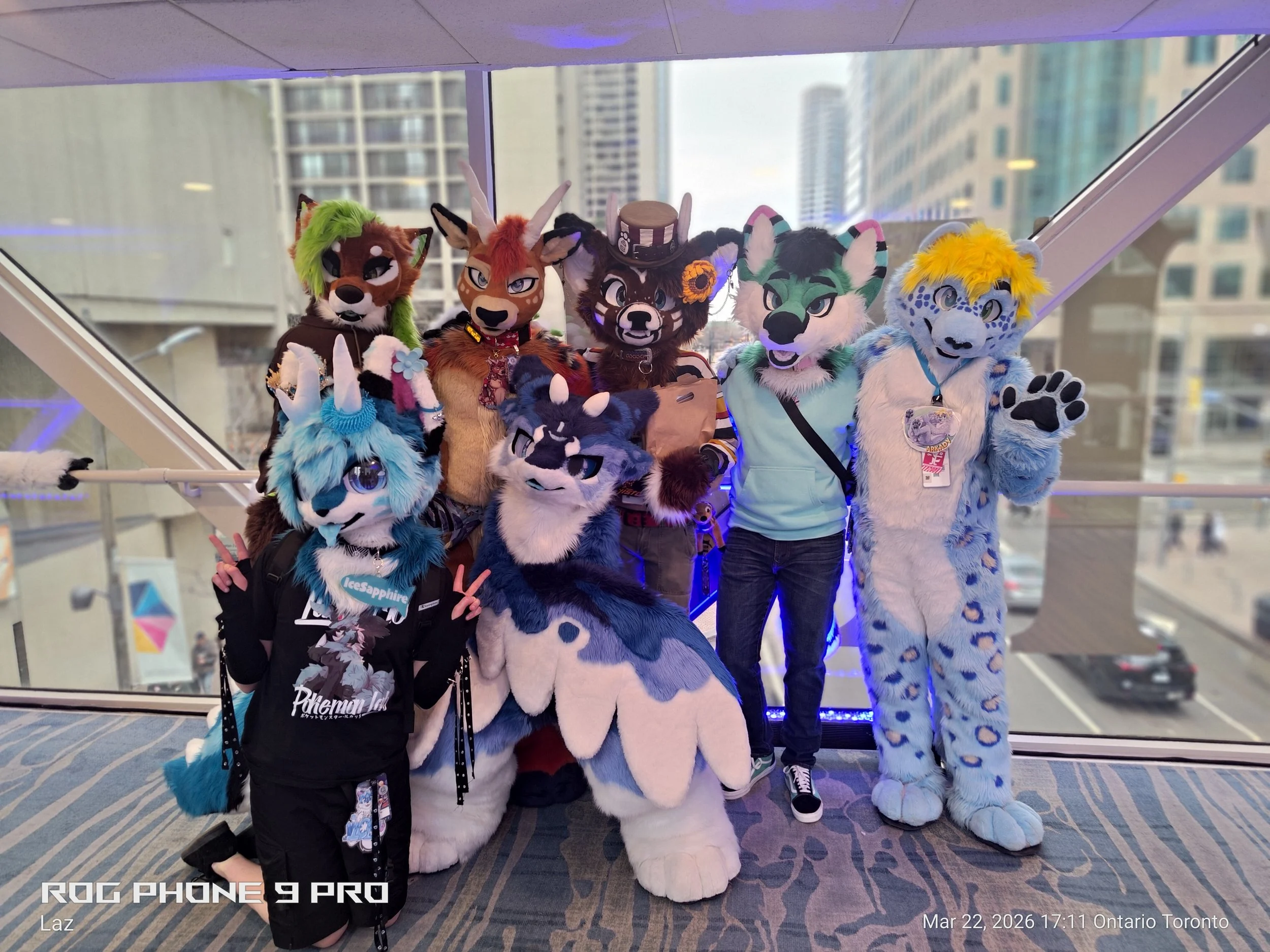 Group of five people in animal costumes posing for a photo in an indoor setting with large windows and city buildings in the background. The costumes include a fox, an antelope, a wild boar, a wolf, and a leopard, all with colorful and detailed desig