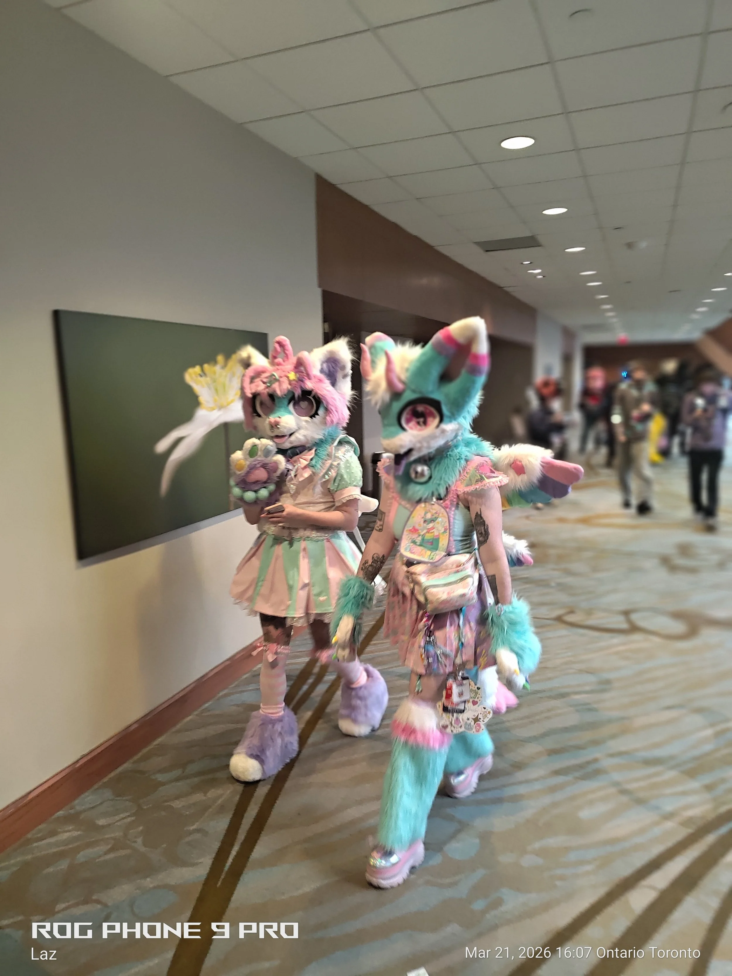 Two individuals dressed in colorful, furry, animal-inspired costumes walking through a hallway at a convention center.